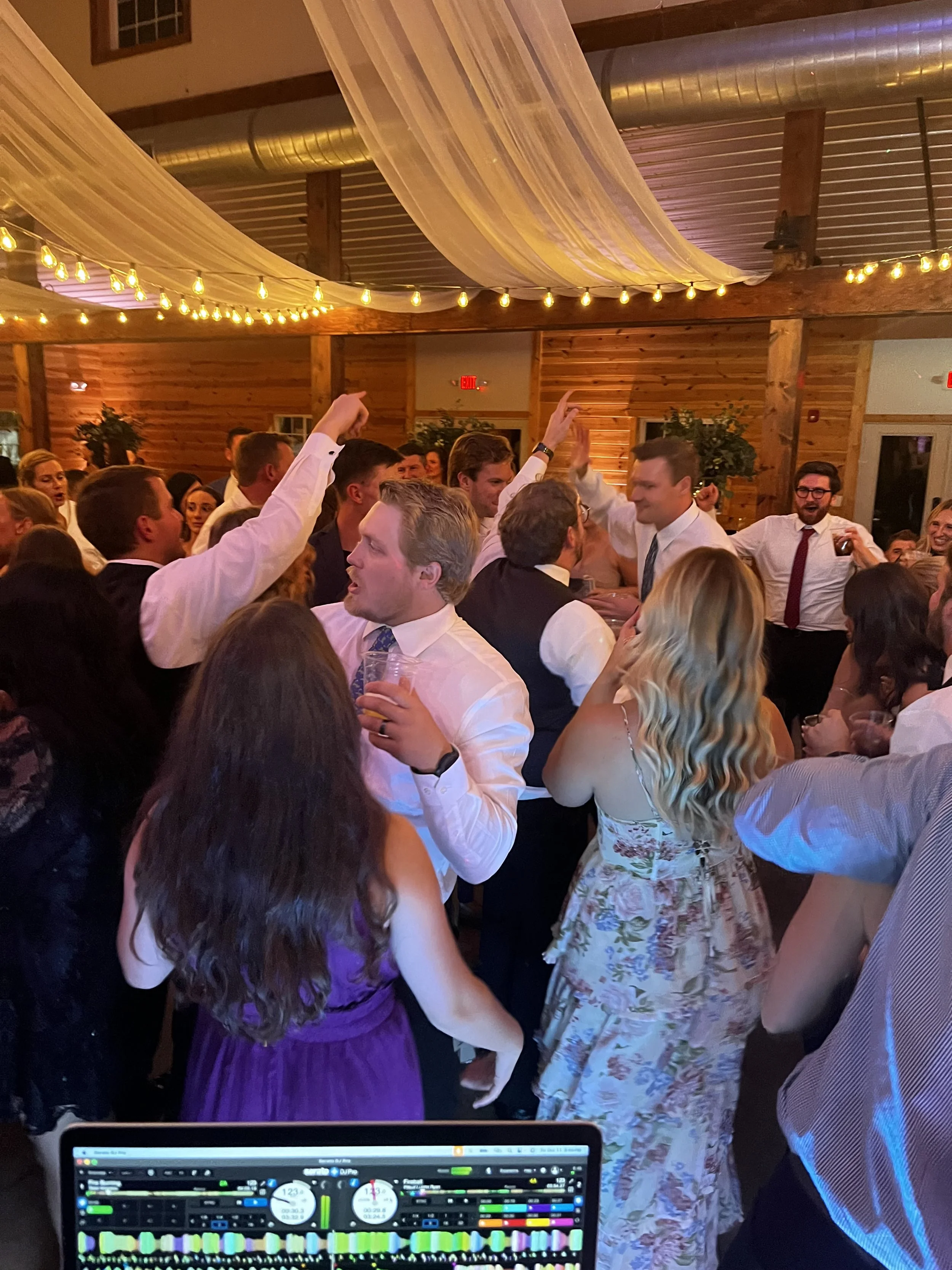 People dancing and socializing at a lively indoor party with string lights and wooden decor.