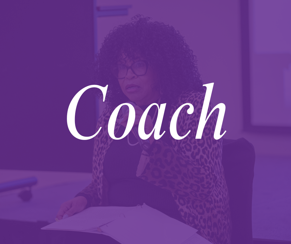 A woman with curly hair and glasses sitting at a table with papers, in a room with a purple overlay, with the word 'Coach' written across the image.
