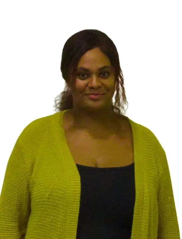 A woman with dark hair, wearing a black top and a yellow cardigan, standing against a white background.