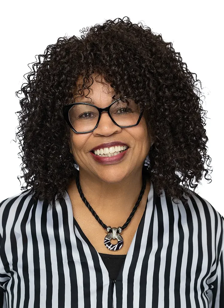 Smiling woman with curly hair, glasses, and striped blazer.