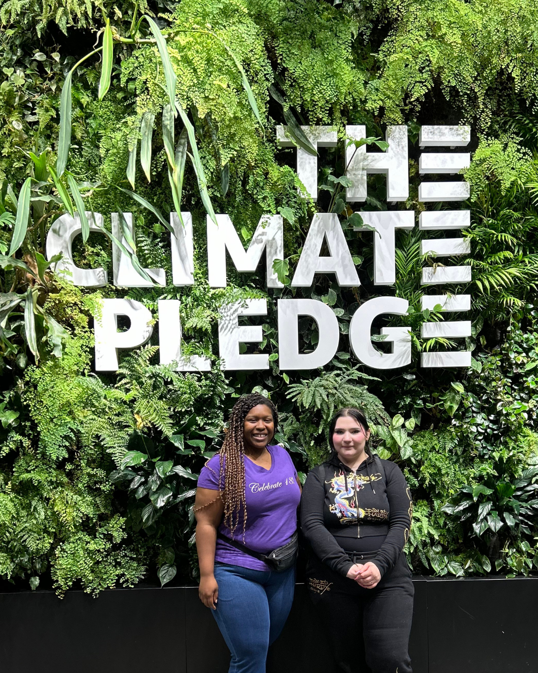Two women standing in front of a green wall with the words 'The Climate Pledge' in large white letters.