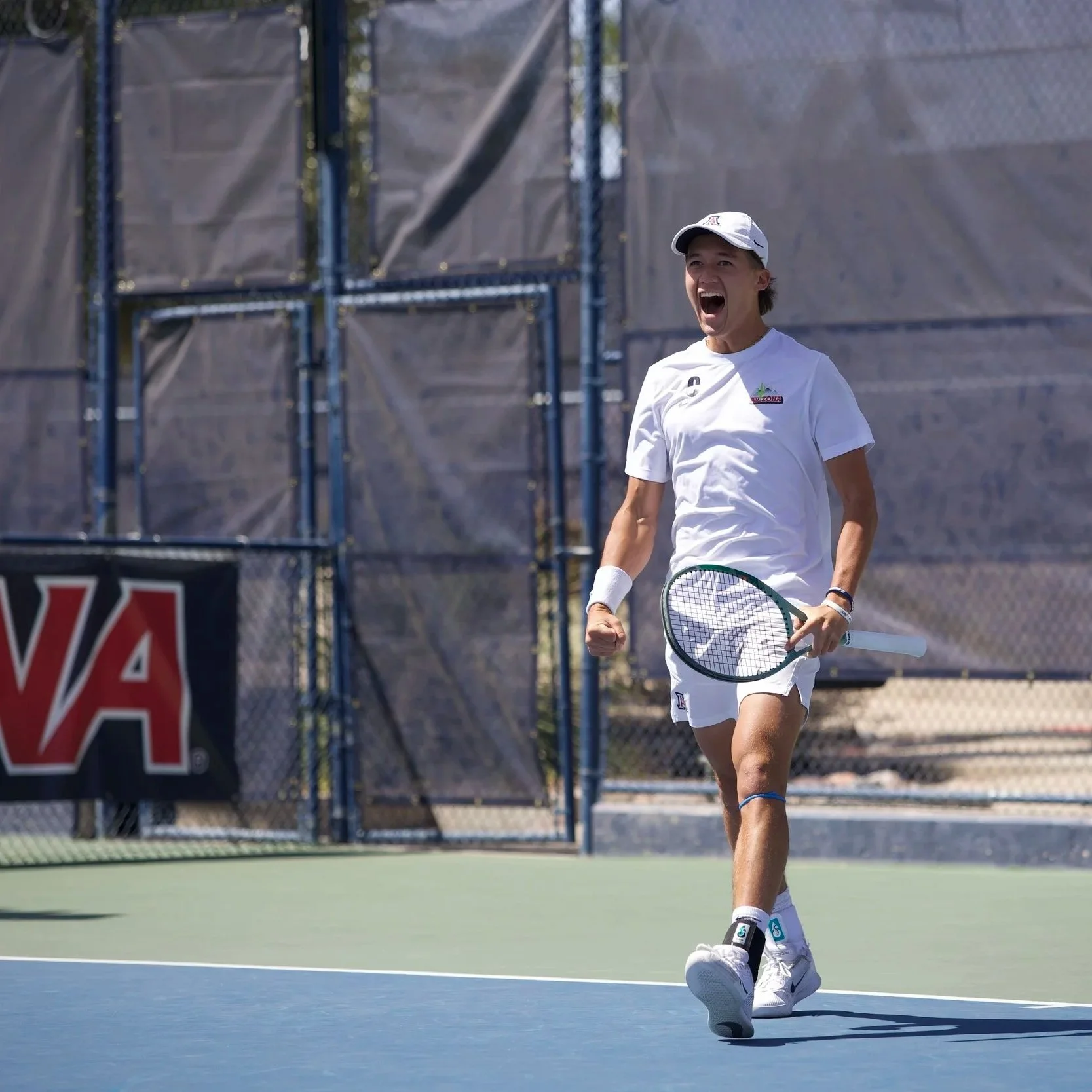 A female tennis player on an outdoor court celebrating with joy, holding a tennis racket in her right hand.