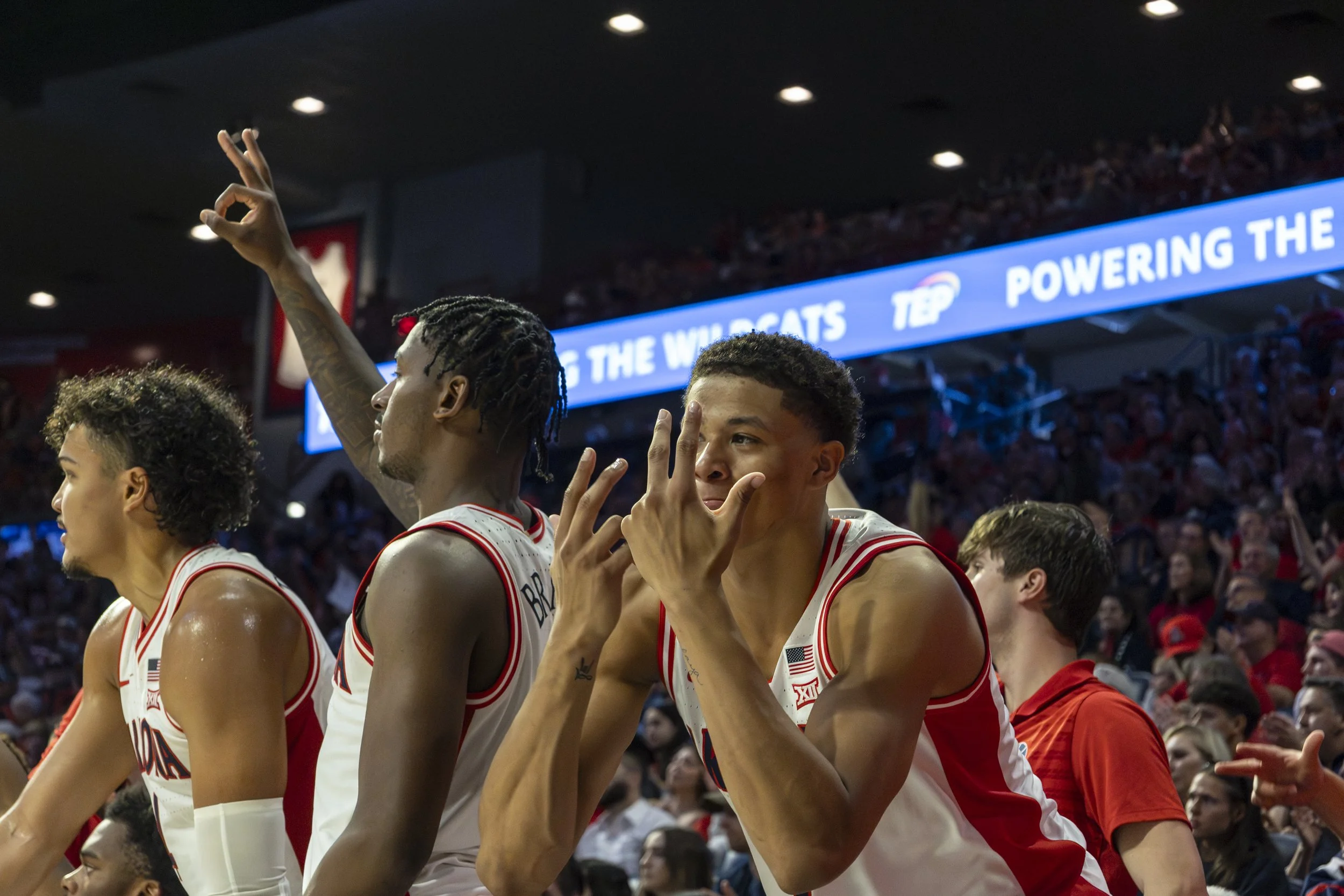 Basketball players wearing white and red uniforms on the court celebrating, with a crowd in the background.