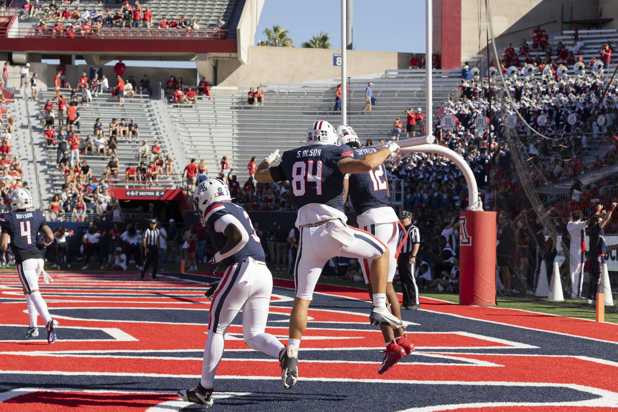 Football players celebrating in front of the end zone at a stadium, with fans in the stands.