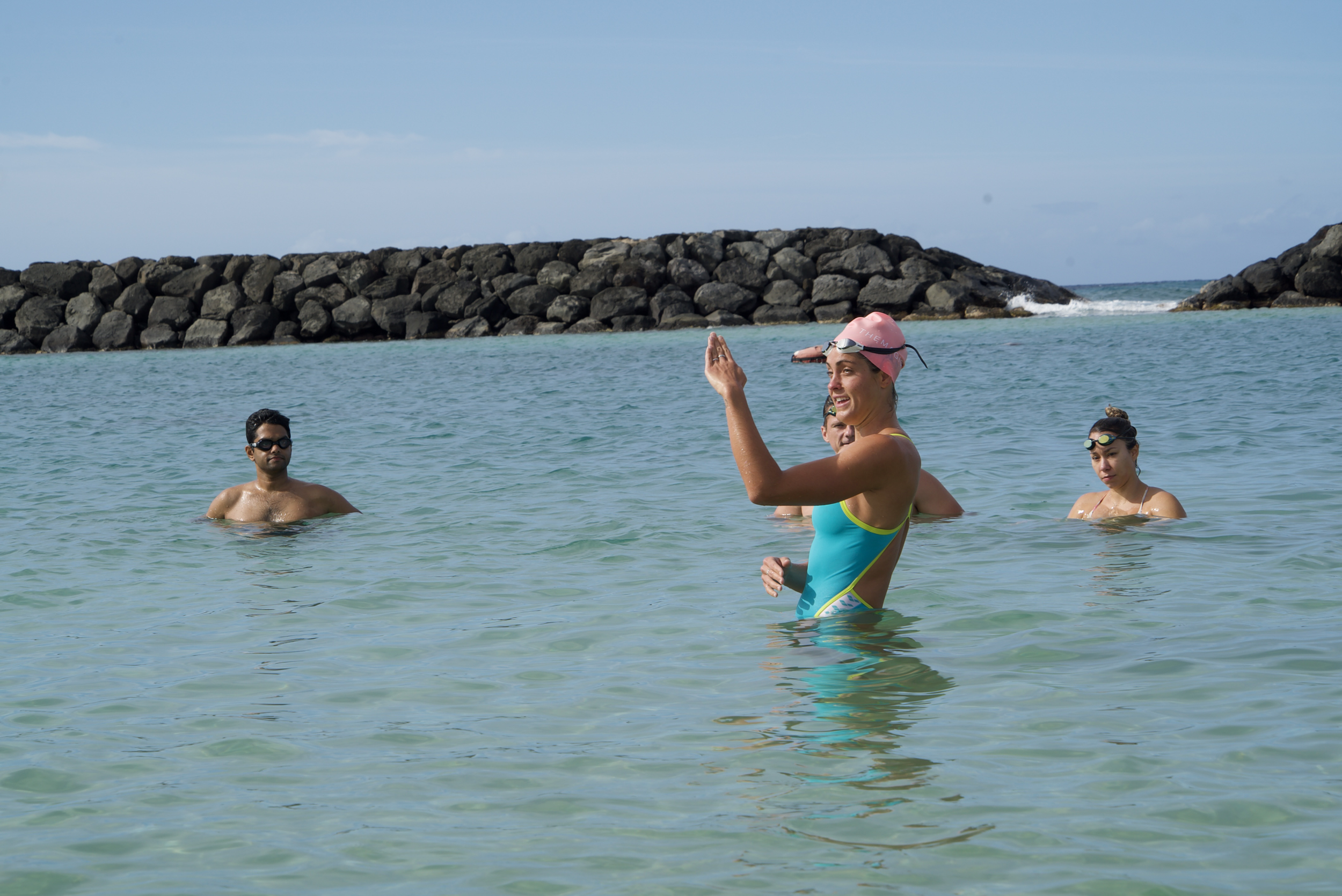 Group of people swimming in the ocean near a rocky breakwater on a sunny day.