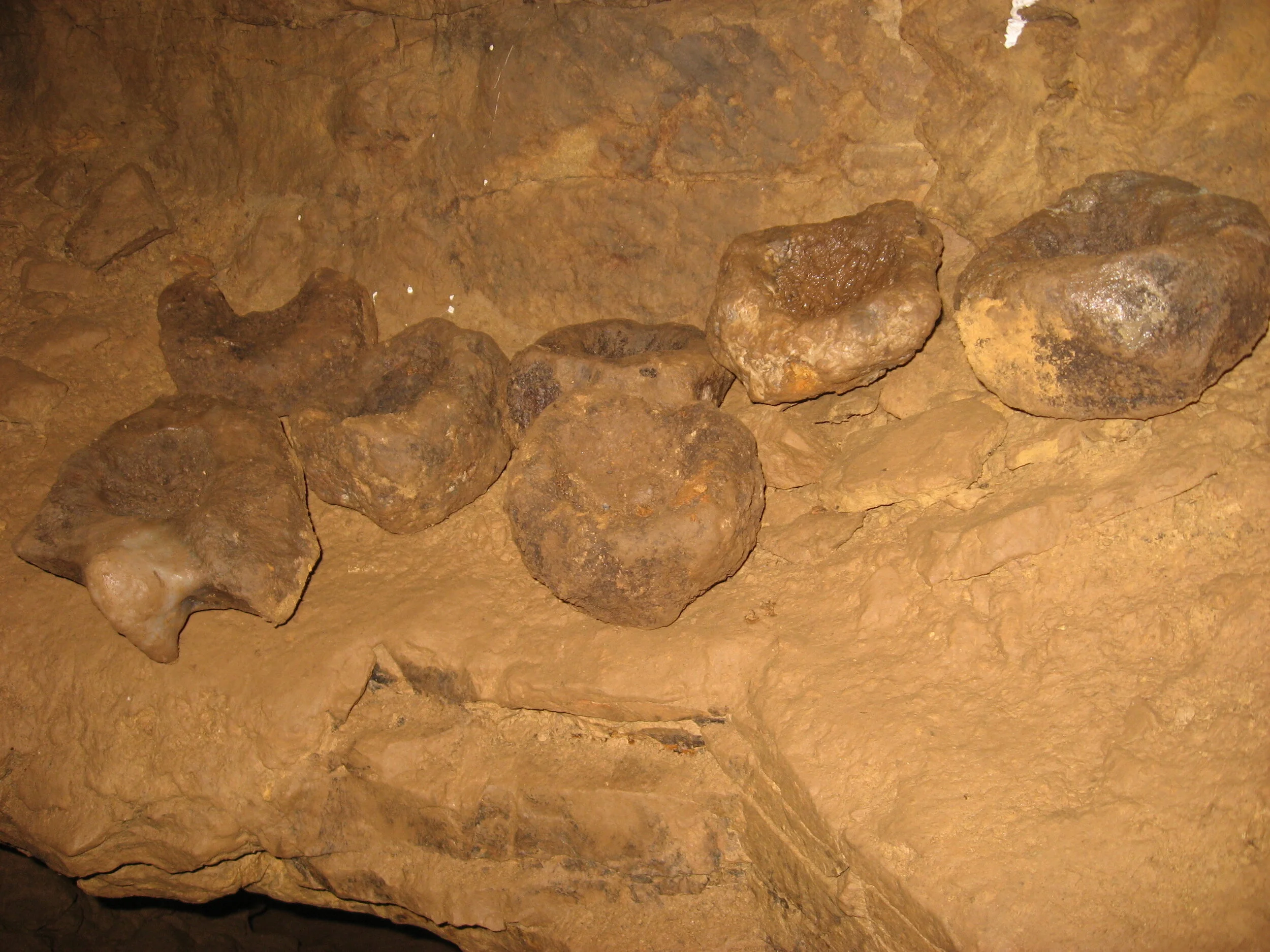 Six large rocks inside a cave or underground space with a sandy or dusty floor.