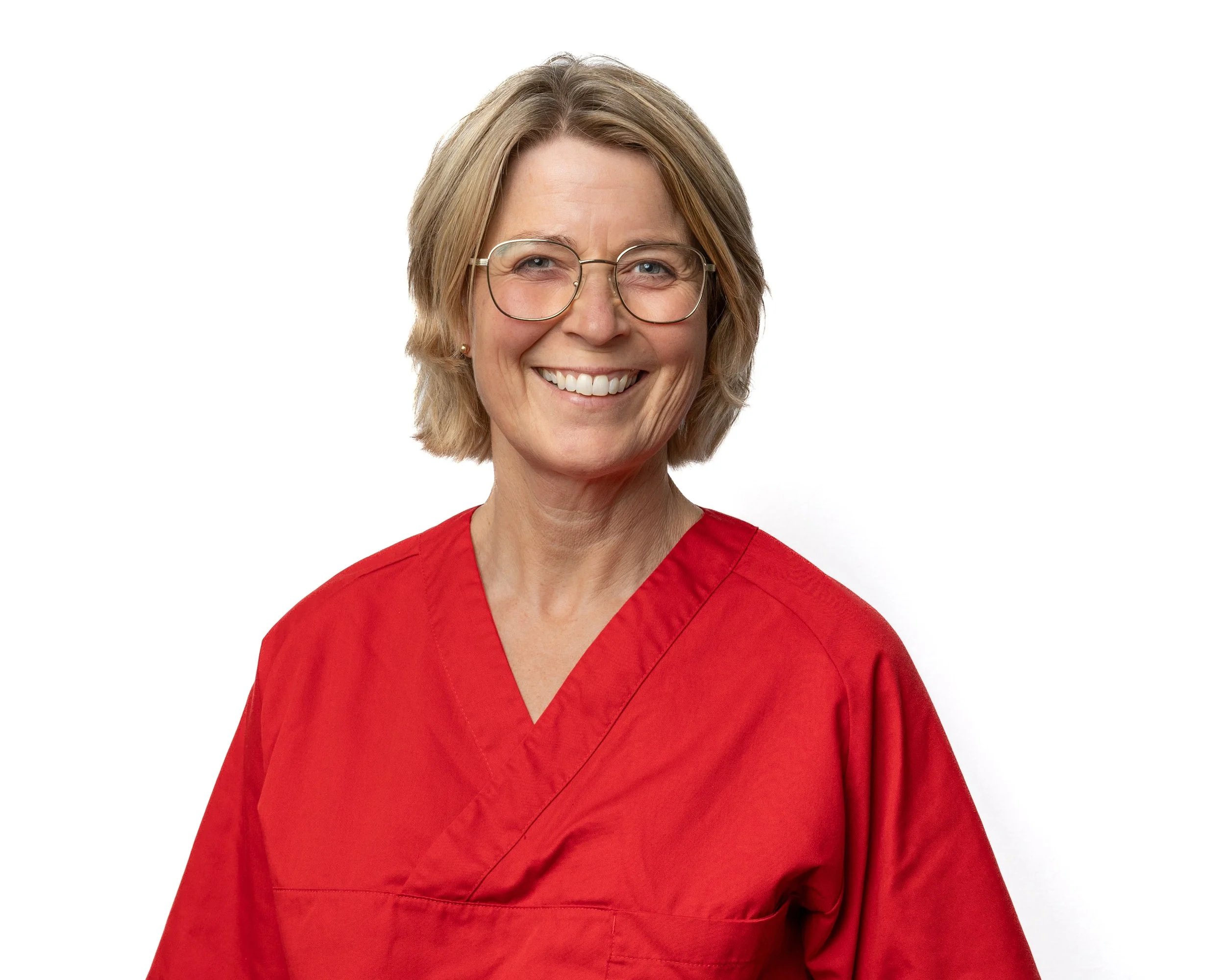 A woman in red medical scrubs smiling and wearing glasses against a white background.