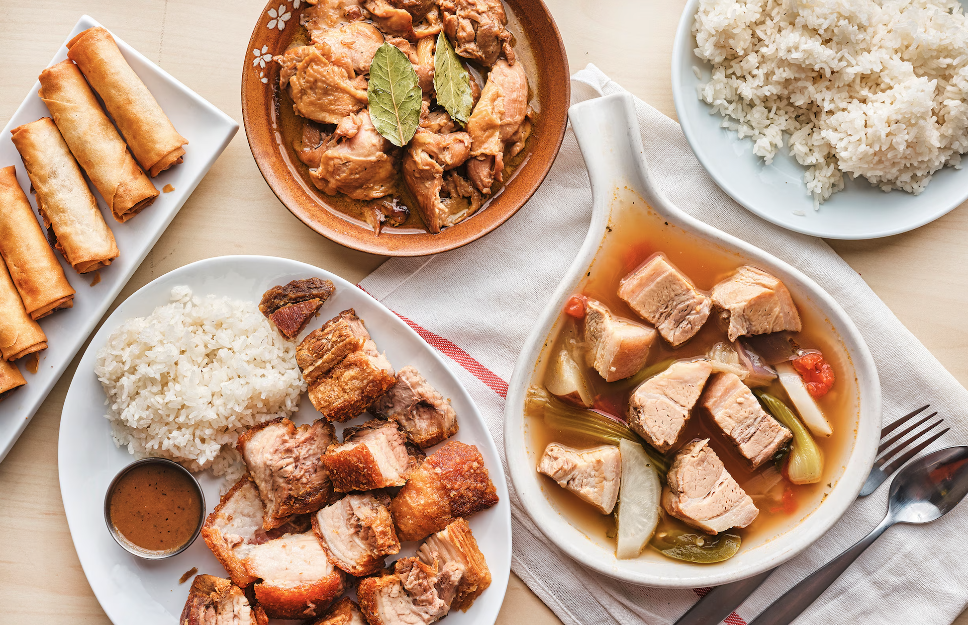An assortment of Asian dishes including spring rolls, fried chicken, rice, and a meat and vegetable stew in a bowl.