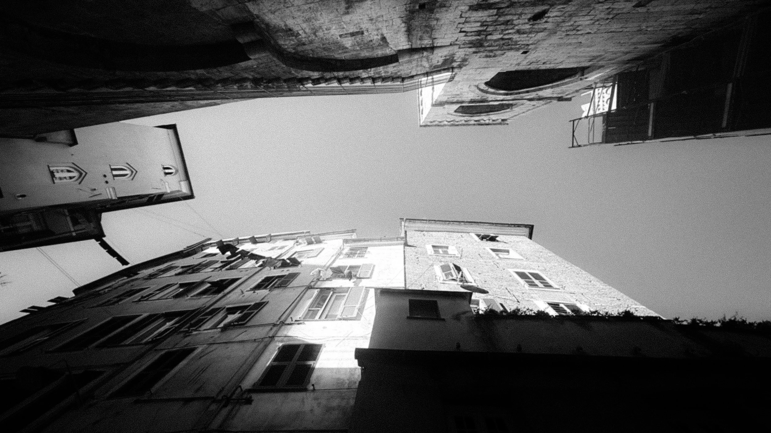 Foto in bianco e nero di edifici di varie altezze visti dal basso, con il cielo visibile sopra di essi.