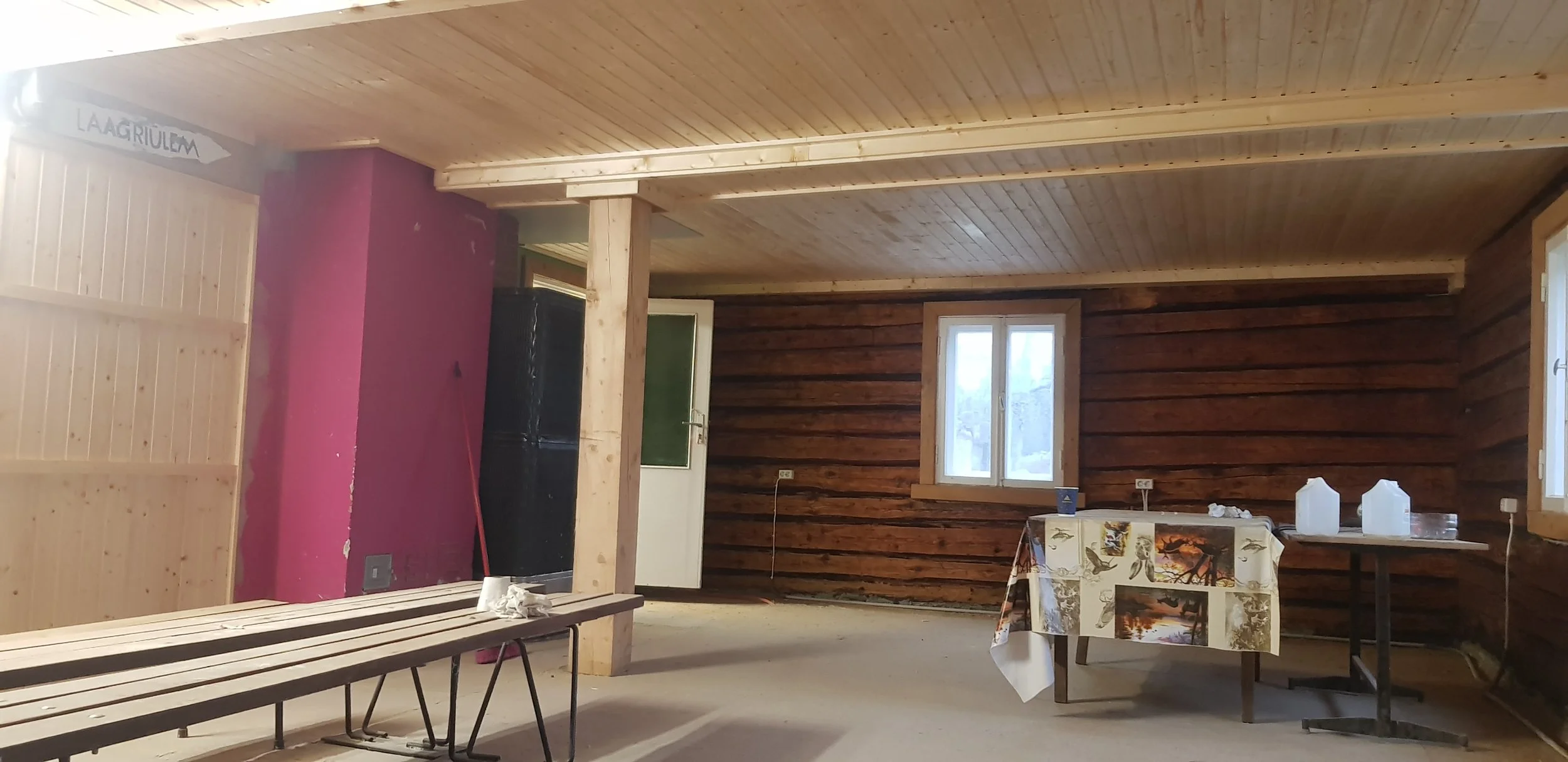 Osaliselt sisustatud tuba, kus lae ja seinte viimistluseks on kasutatud sisevoodrilauda. Puitvooder annab ruumile sooja ja looduslähedase ilme. Toas on laud loodusteemalise linikuga, mõned plastkastid ja aken, mis laseb valgust sisse, kuid keskne rol