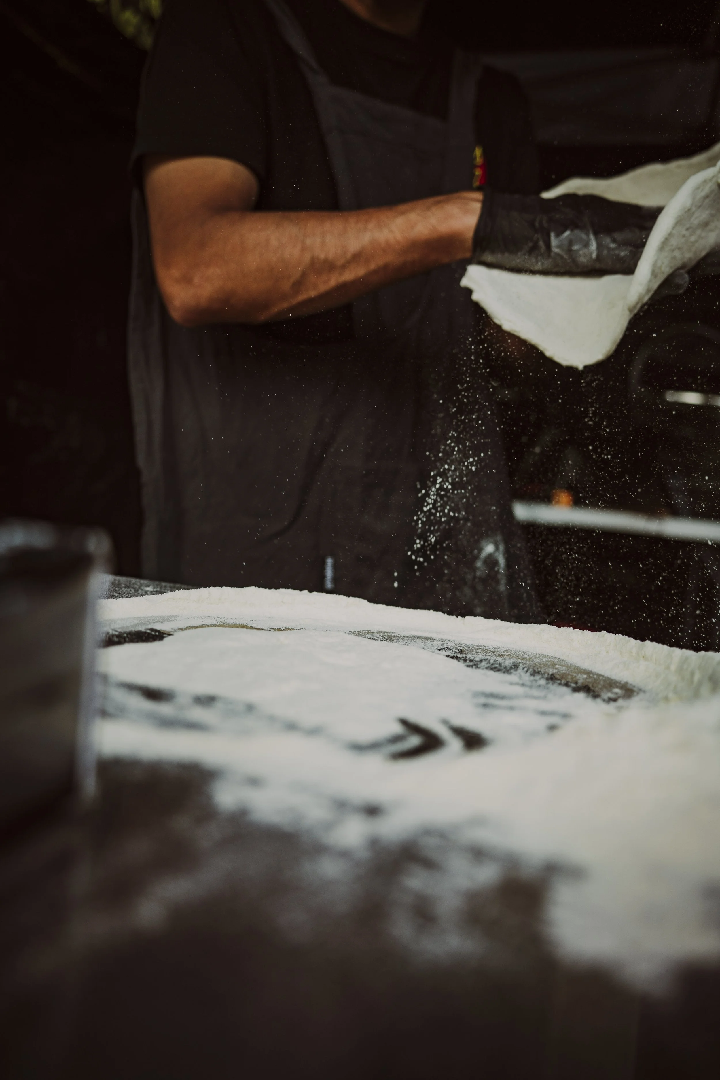 Handmade pizza preparation: Chef slapping fresh dough with flying semolina for a perfect stonebaked crust in Crawley.