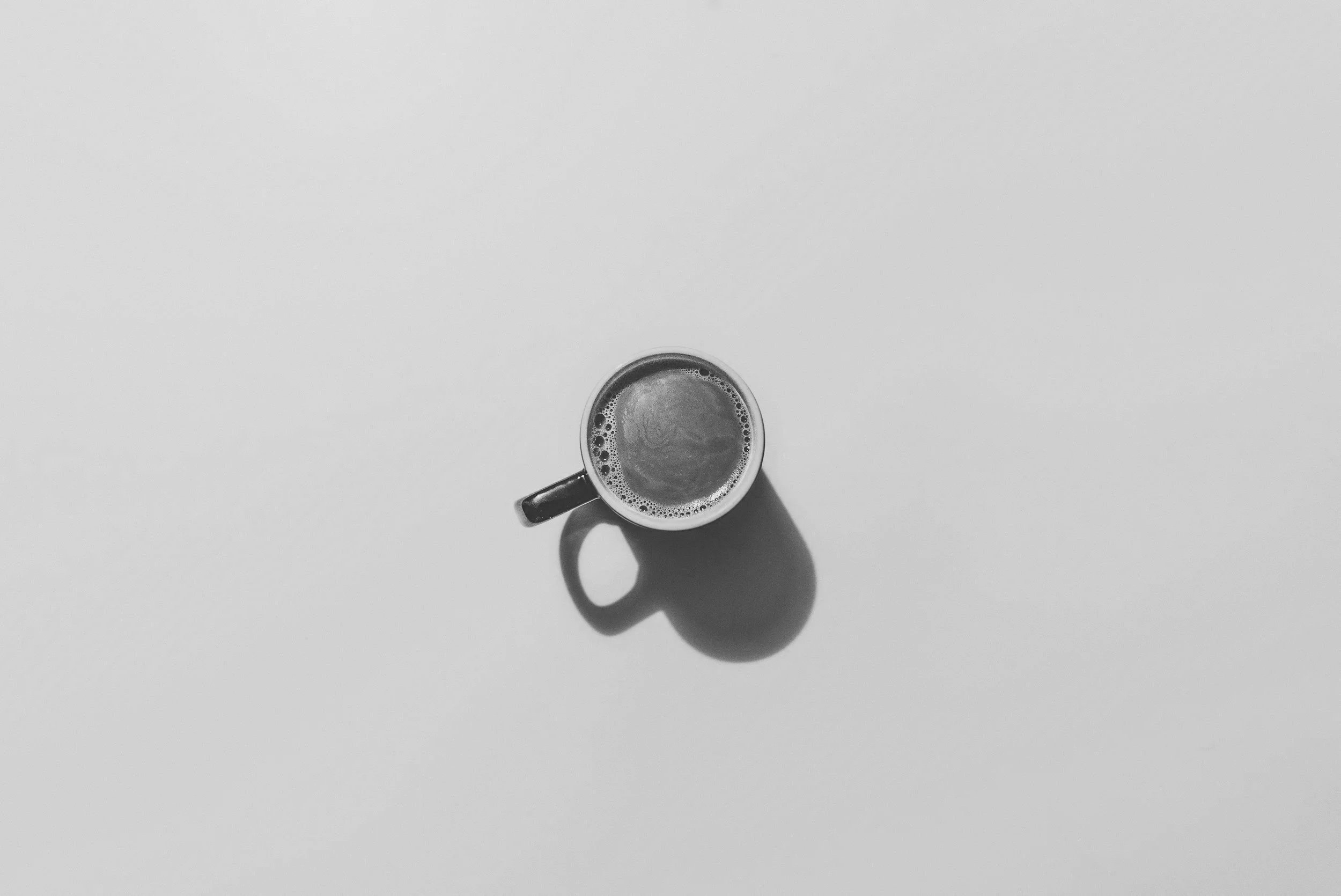 Taza de café en una mesa blanca, vista desde arriba, con sombra.