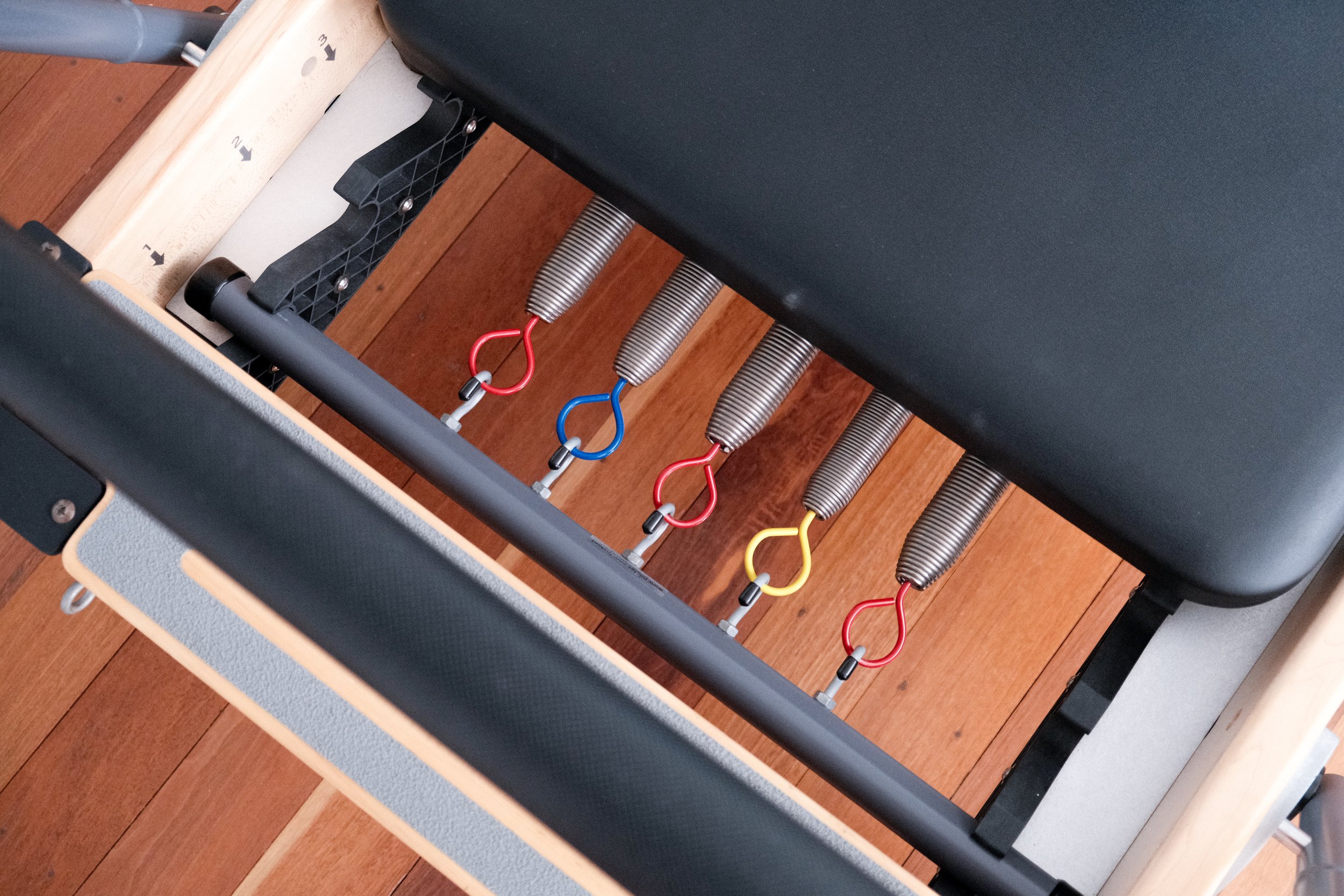 View of a chiropractic or massage table with adjustable metal springs and colored hooks attached to the frame.