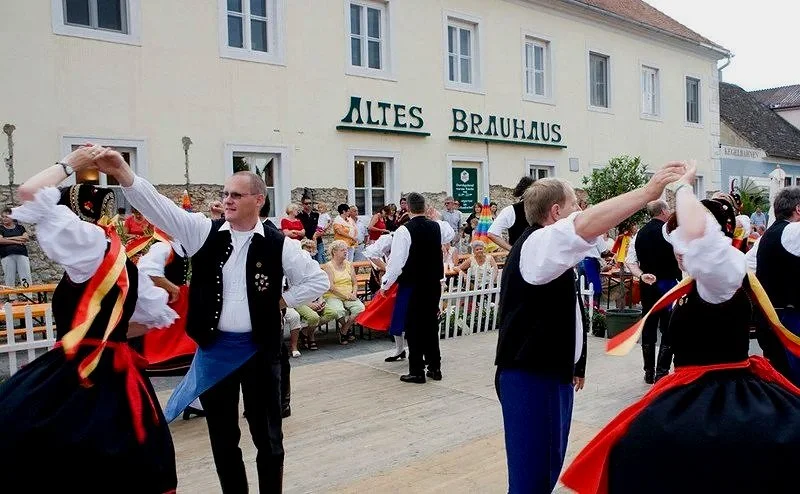 Traditionelle deutsche Tänzer in Tracht tanzen vor einem Publikum bei einem Fest vor einem Gebäude mit 'Altes Brauhaus'-Schild.