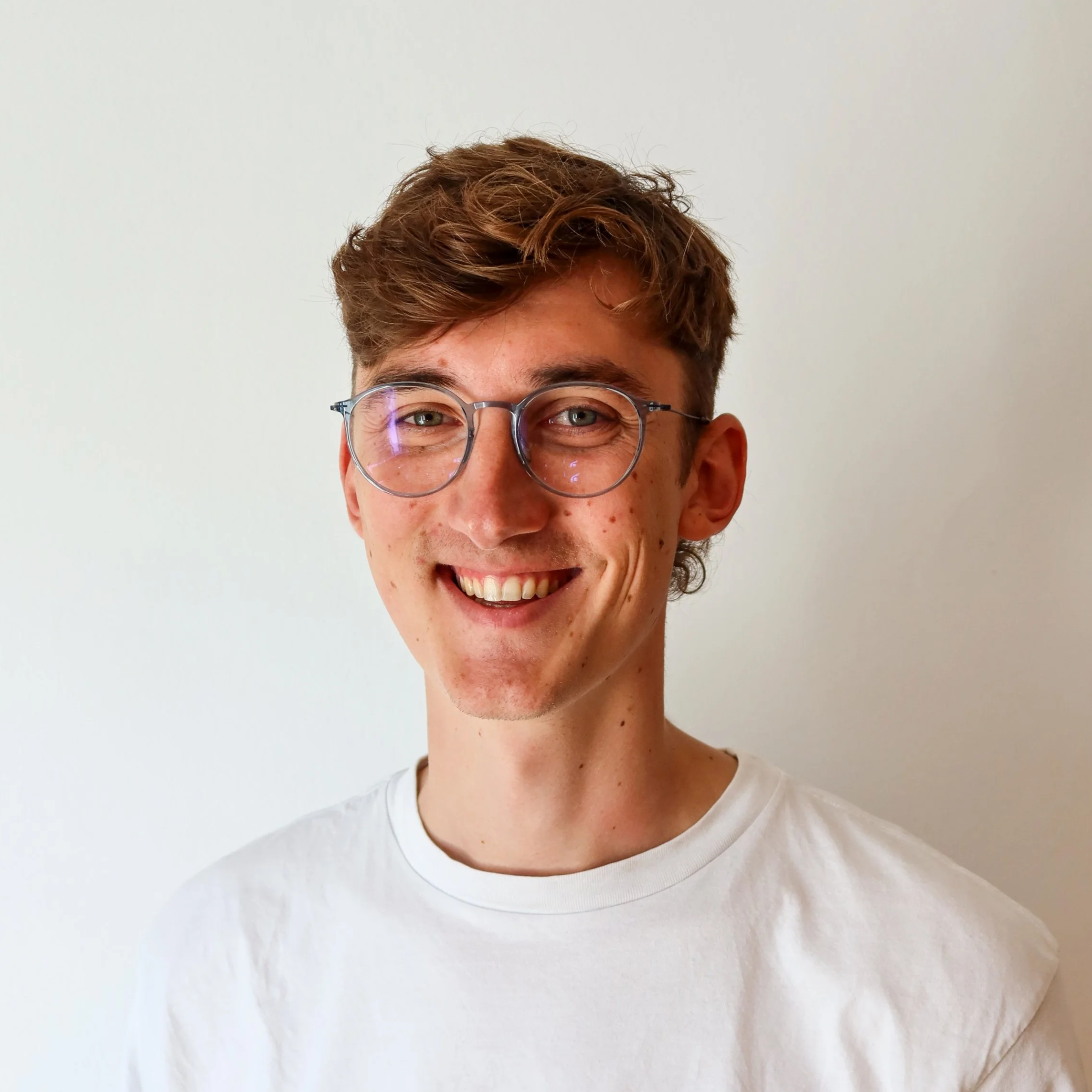 Lächelnder junger Mann mit Brille und weißen Hemd vor weißem Hintergrund.