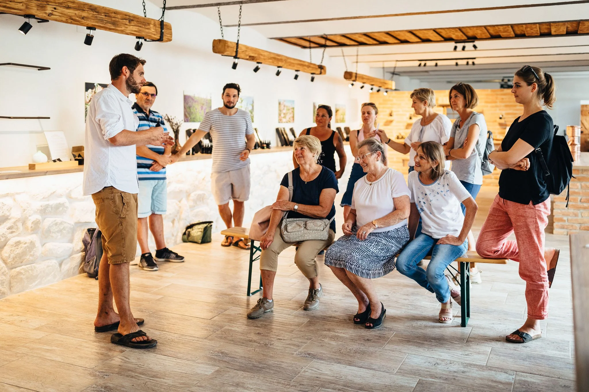 Eine Gruppe von Menschen sitzt und steht in einem modernen Raum und hört einem Mann zu, der einen Vortrag hält.