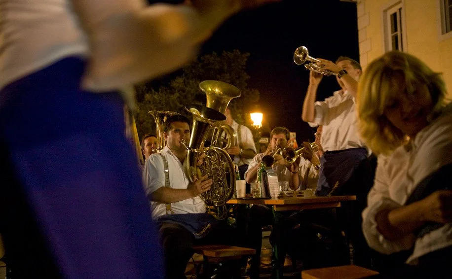 Musiker einer Blasmusikkapelle spielen nachts auf einer Straße oder einem Platz, mit Beleuchtung durch Straßenlaternen.