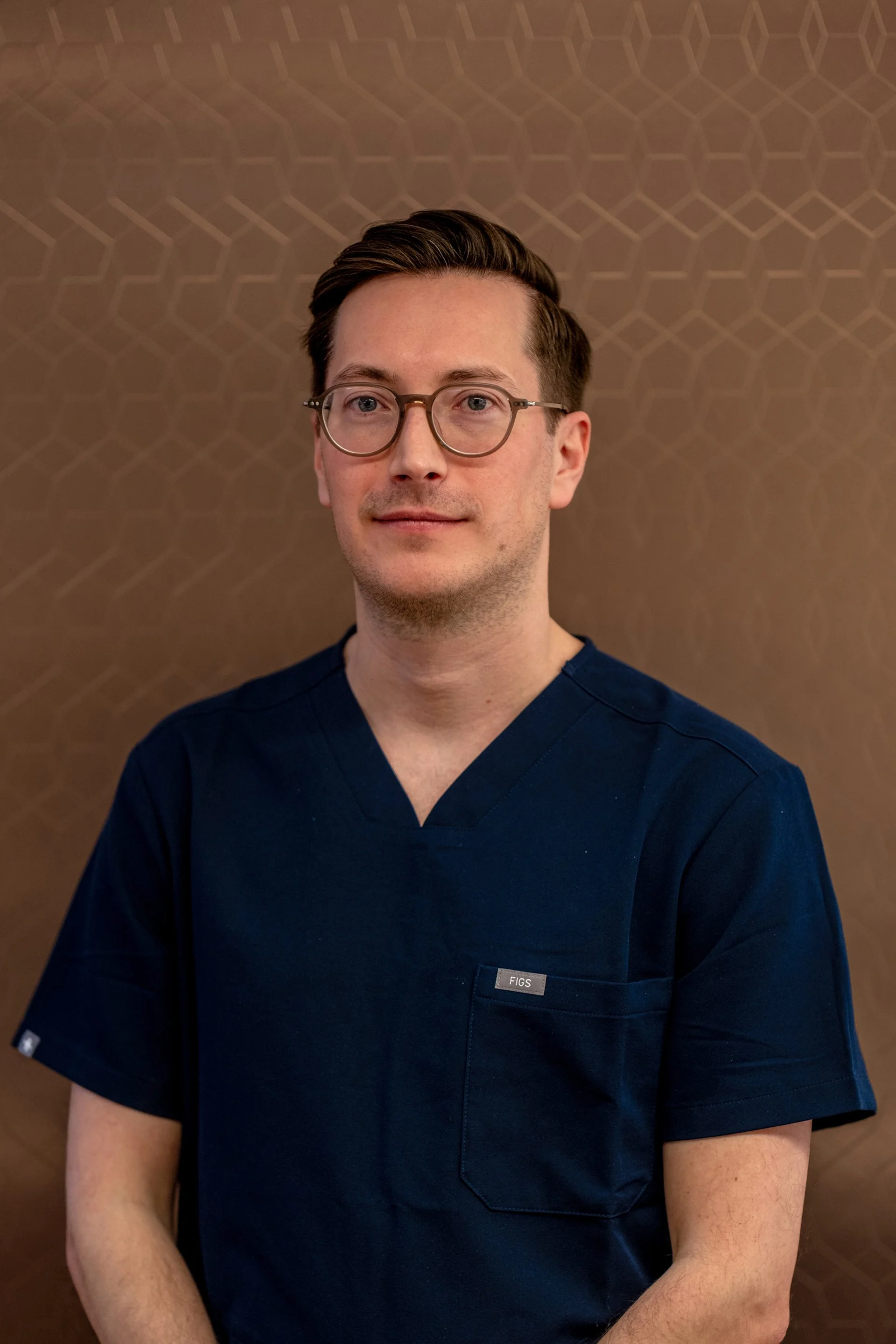 Mann in blauer medizinischer Uniform vor braunem Hintergrund.