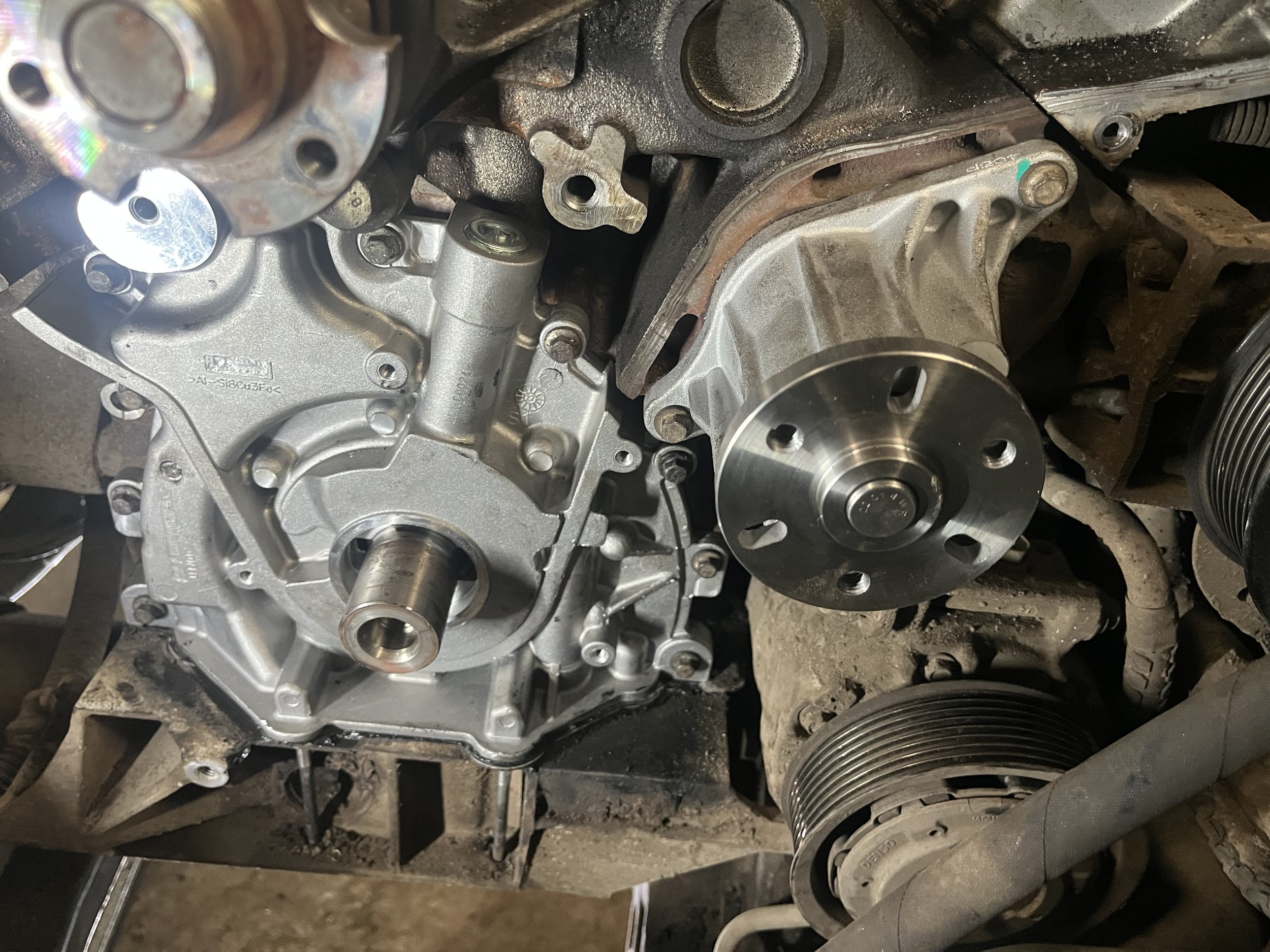 Zicht op een motorblok met een nieuw geïnstalleerde waterpomp, waarbij de distributieriempoelie en andere motoronderdelen zichtbaar zijn.