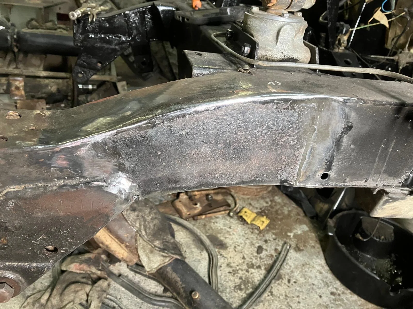 Close-up van het chassis en de ophangingscomponenten van een voertuig tijdens herstelling, met roest en vuil op de metalen onderdelen.