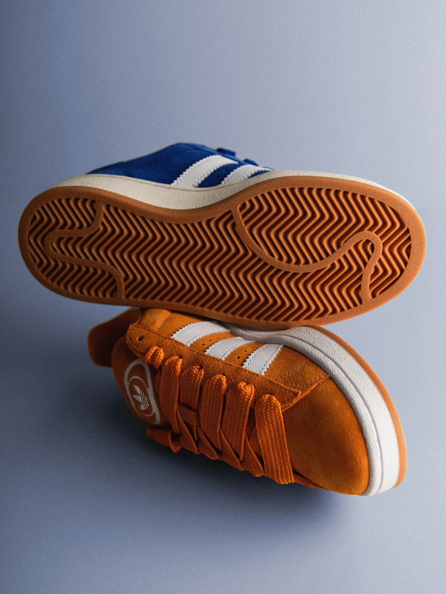 Nahaufnahme eines Sneakers, der Kopf nach oben zeigt, mit orangefarbenem Obermaterial, weißen Streifen und Gummisohle auf einem grauen Hintergrund.