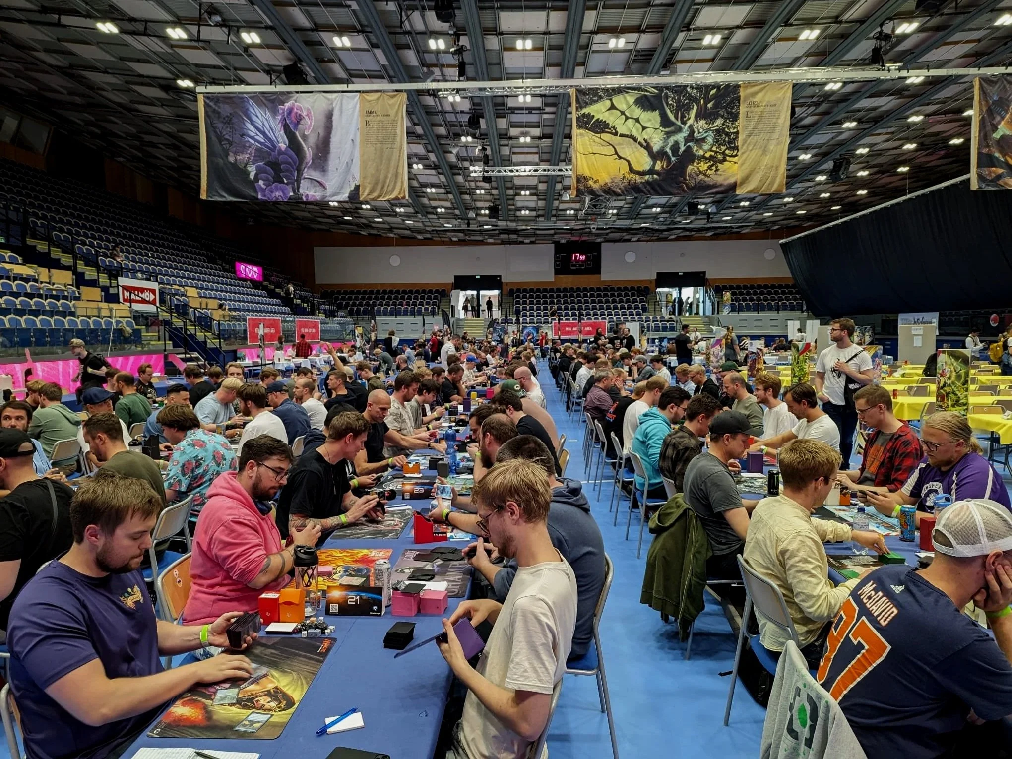 A lot of people sitting in a hall and playing trading card game called Magic The Gathering.