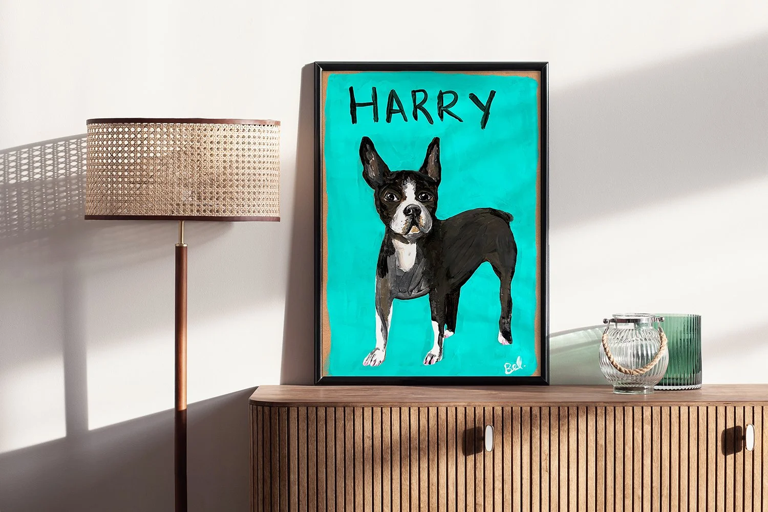 A framed painting of a Boston Terrier dog with the name 'HARRY' on a turquoise background, placed on a wooden sideboard. To the left, there is a standing lamp with a woven shade, casting a shadow on the wall. To the right, there is a glass jar with a rope handle and a green glass container.