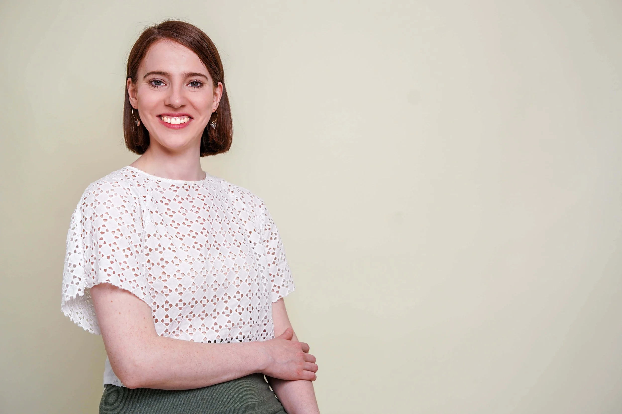Sophie Dean Decluttering Expert and Professional Organiser with shoulder length brown hair and wearing a white cut out top, smiling and holding her right hand on top of her left arm.