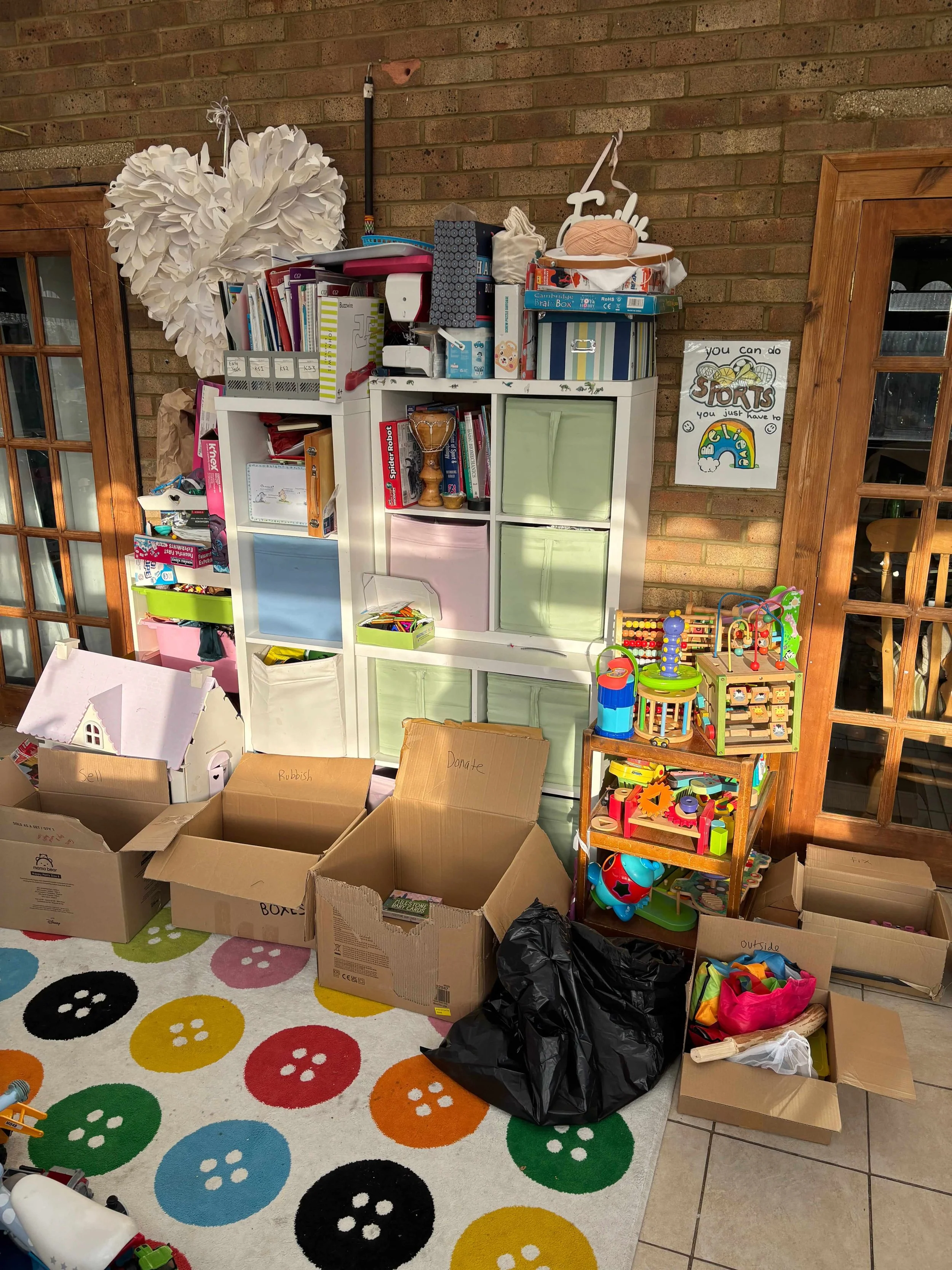 A messy children's playroom with boxes laid down for a decluttering session, labelled donate, recycle and outside.