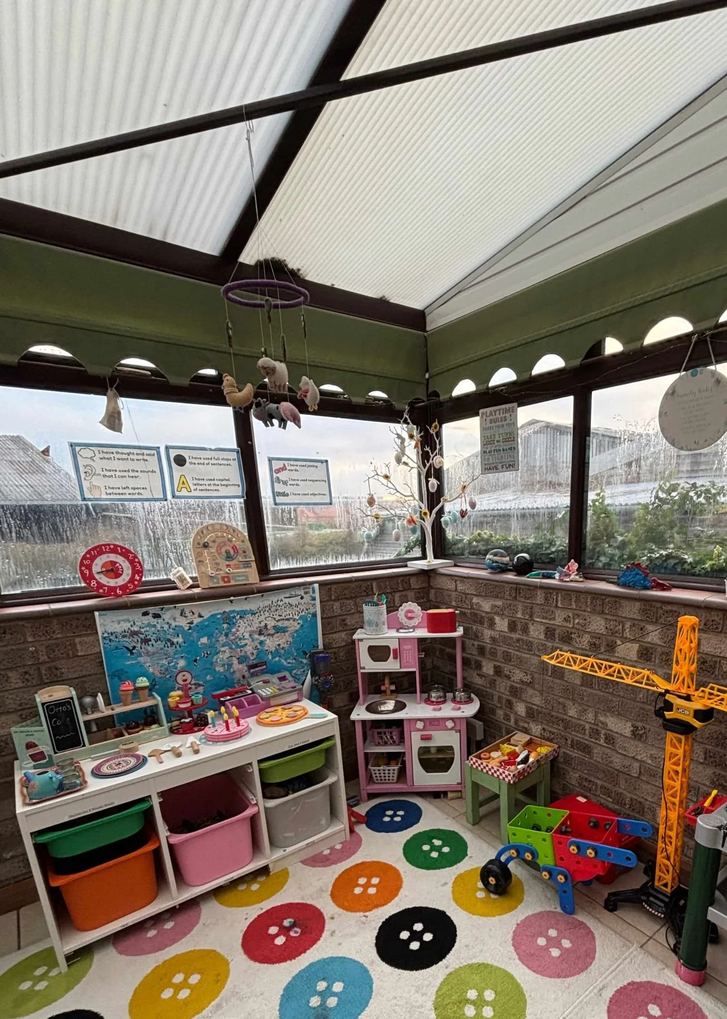 An organised corner of a children's playroom with a play kitchen with wooden furniture, white storage boxes with pull out drawers and construction toys.