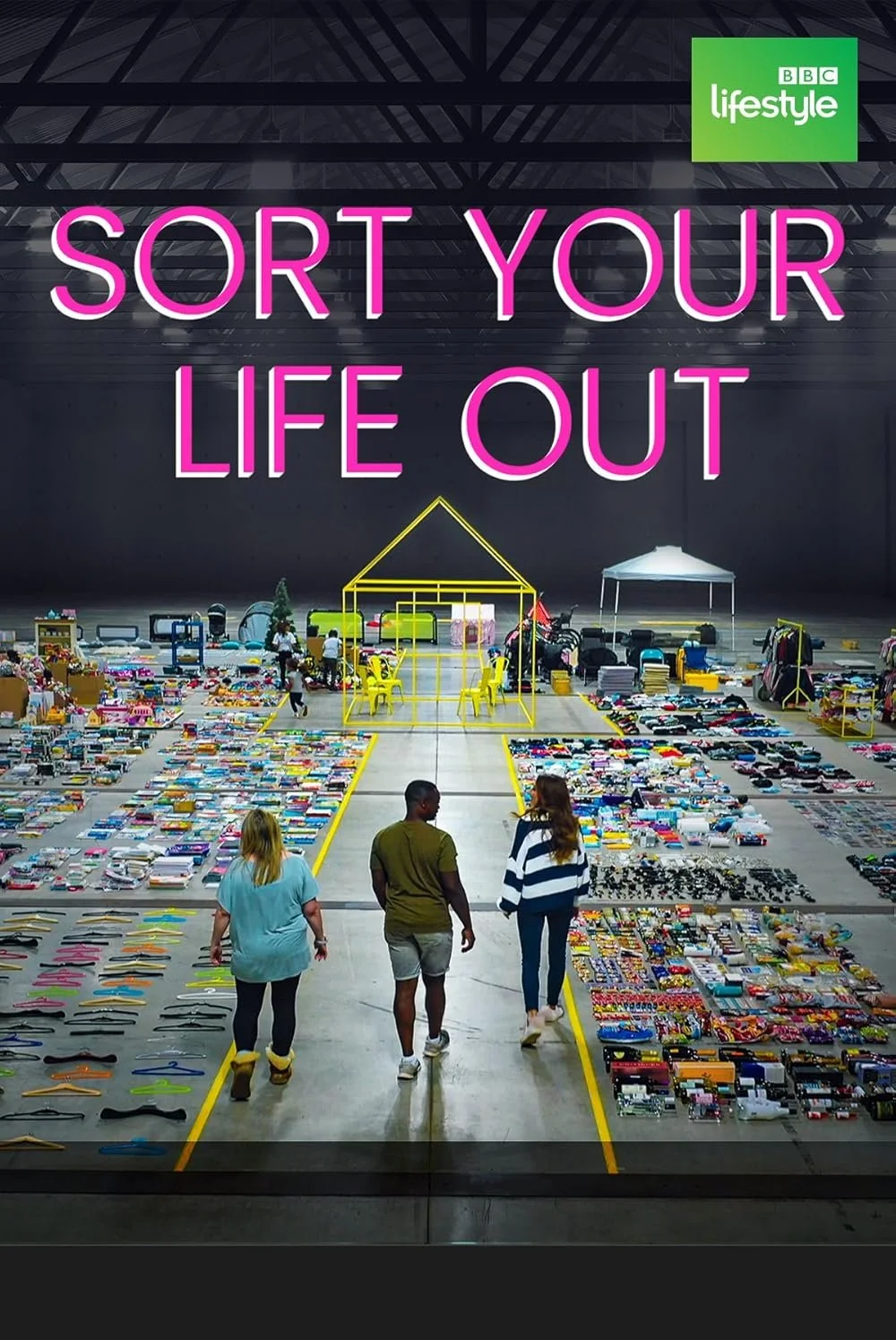 Three people standing in a warehouse looking at tables and piles of assorted categorised items, including toys, clothes, and accessories. Neon text saying 'Sort Your Life Out' and a green BBC Lifestyle logo are displayed above.