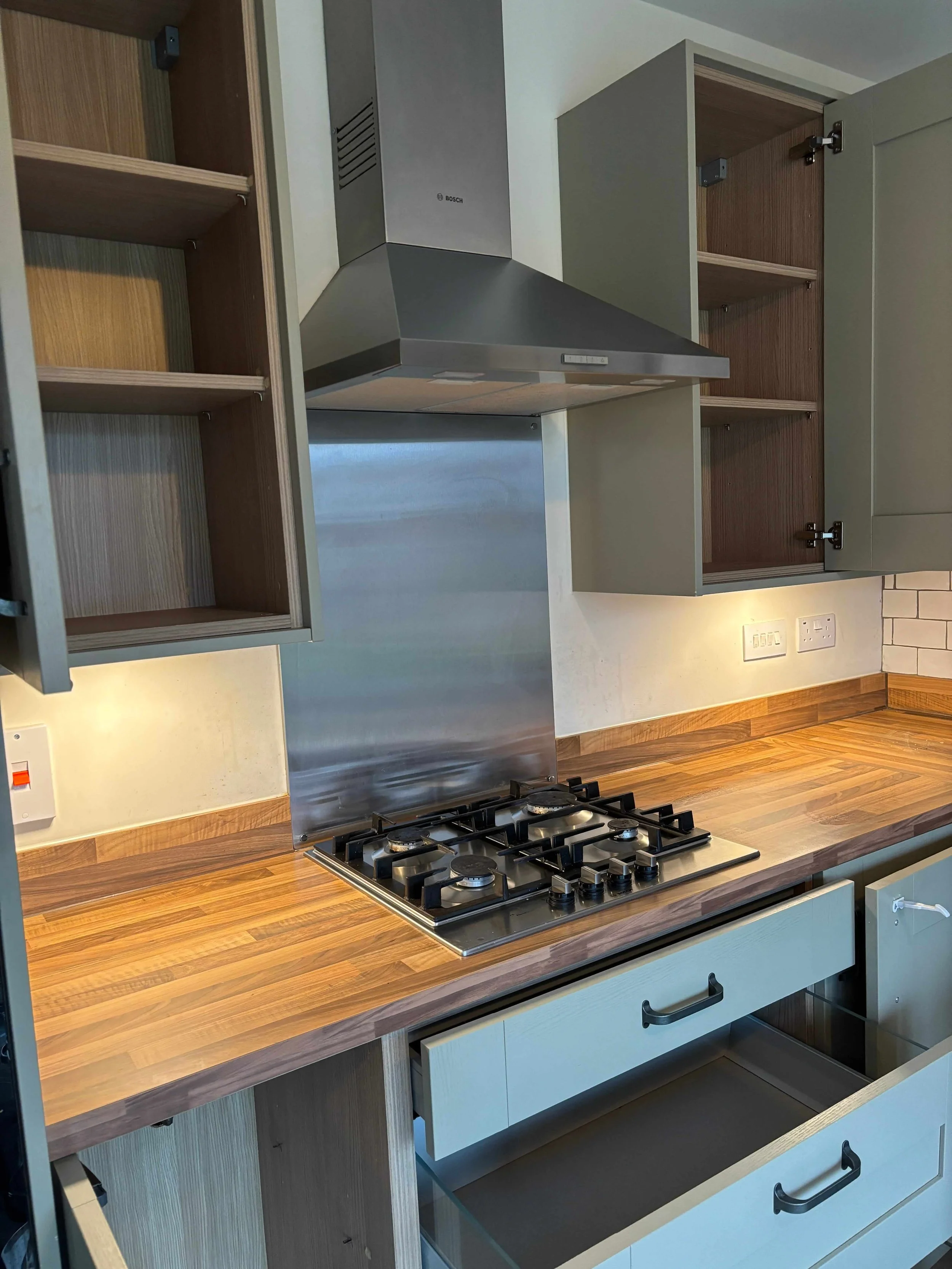 Modern kitchen with wooden countertops, open shelves, wall-mounted oven hood, and built-in gas hob with four burners.