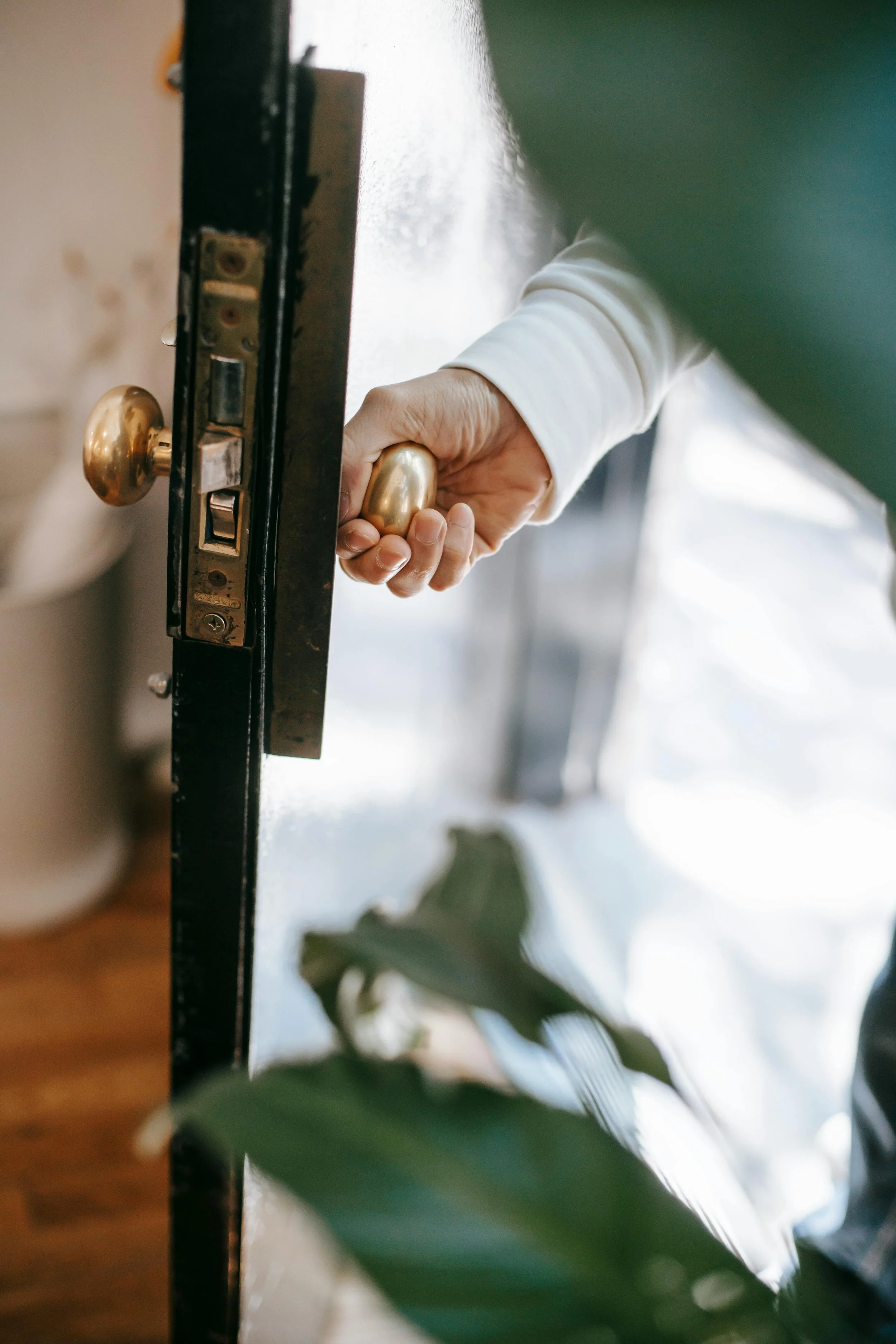 Person opening a door with a gold-coloured doorknob, viewed from the side.