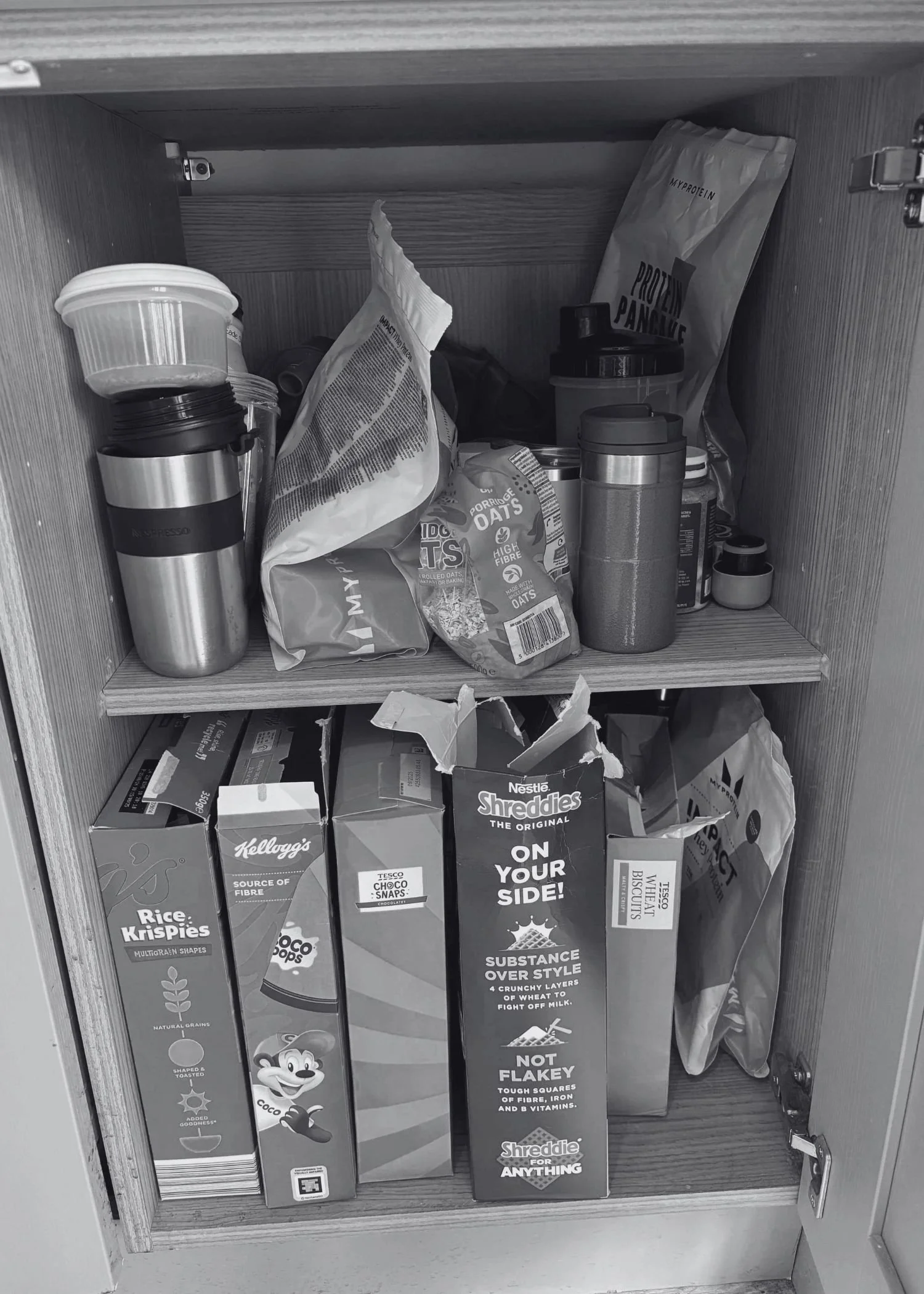 A messy kitchen cupboard with breakfast cereals, metal cups and protein powders in it.