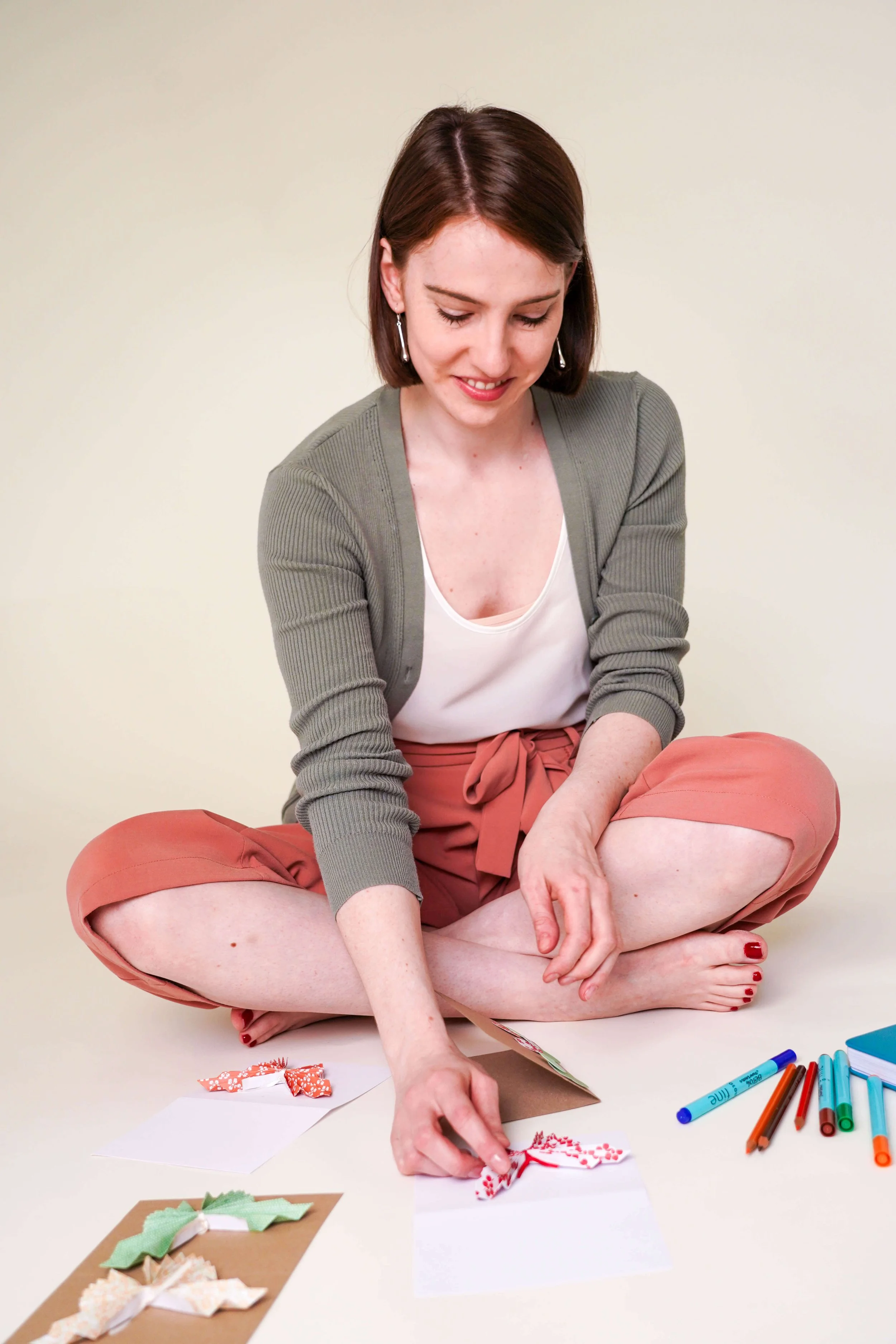 Sophie Dean Decluttering Expert and Professional Organiser with shoulder length brown hair sitting cross-legged on the floor, smiling, making handmade butterflies and markers nearby.