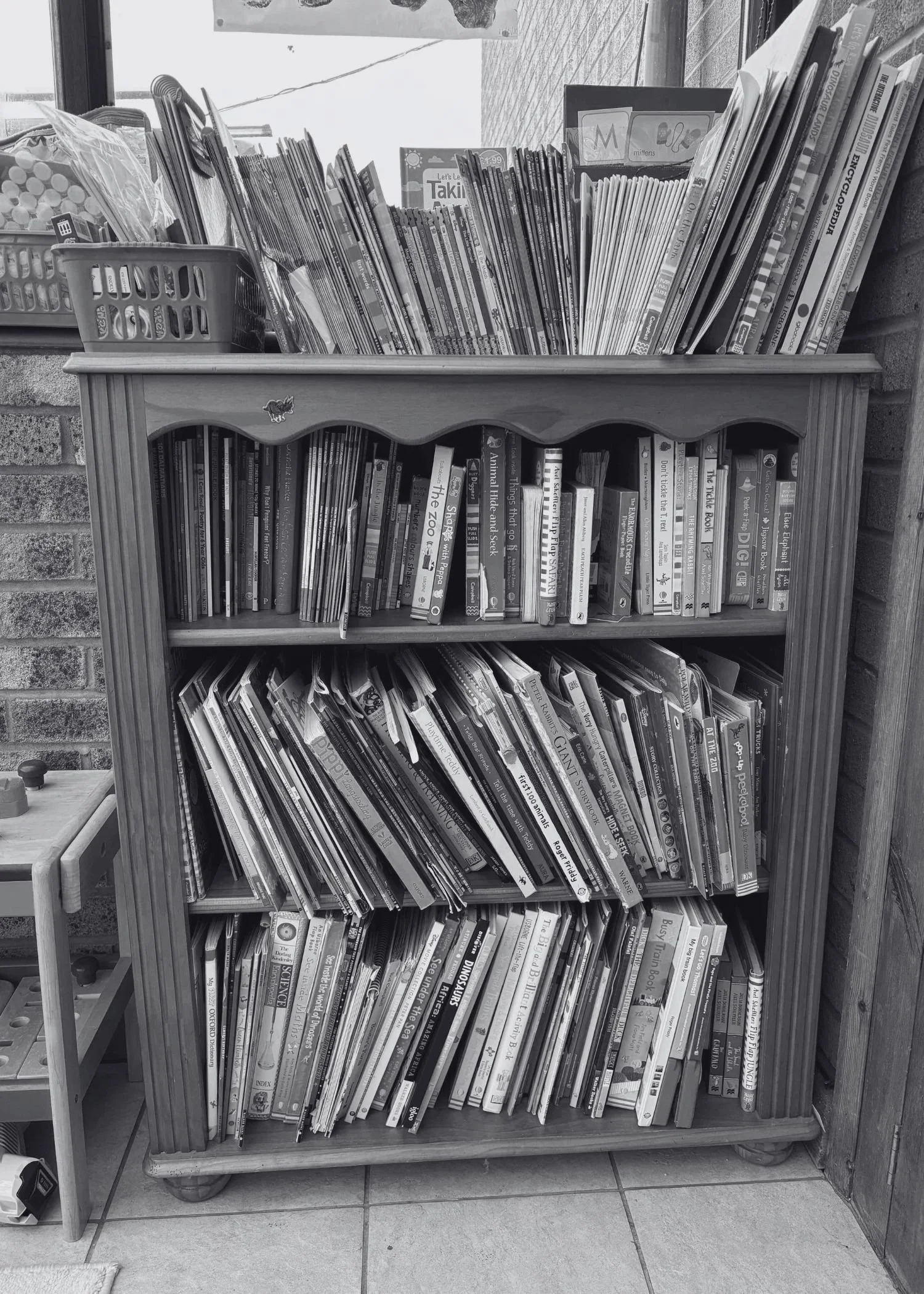 A messy bookshelf in a children's playroom with different sized books on it.