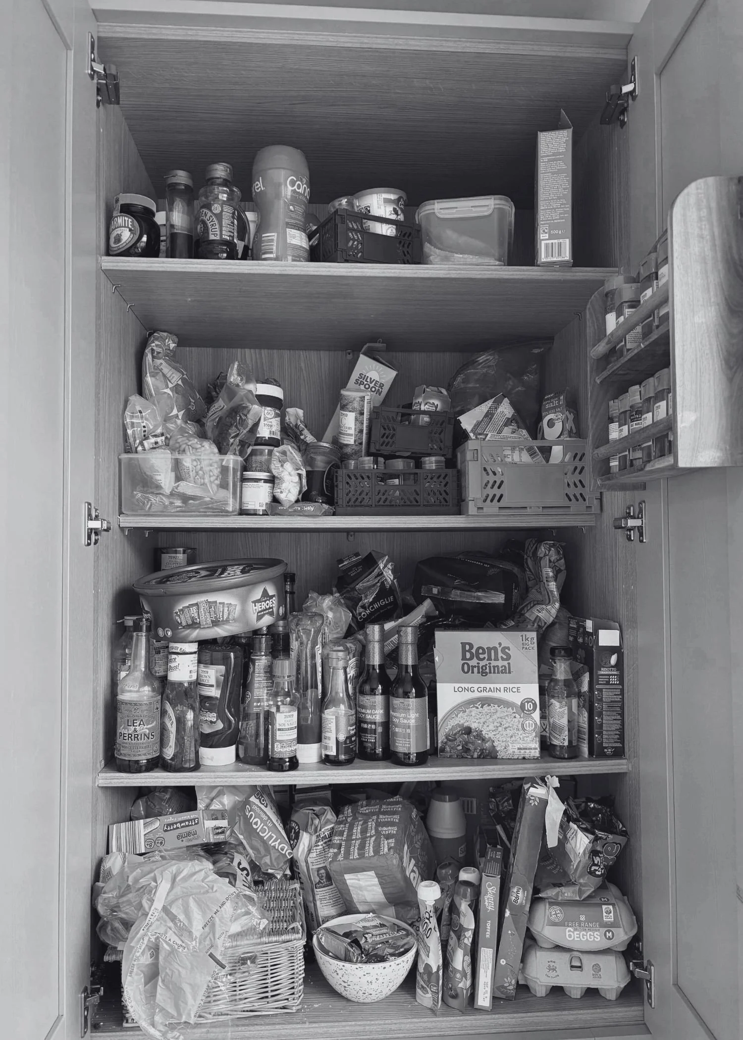 An unorganised messy pantry in a kitchen with stuffed shelves full of different foods.