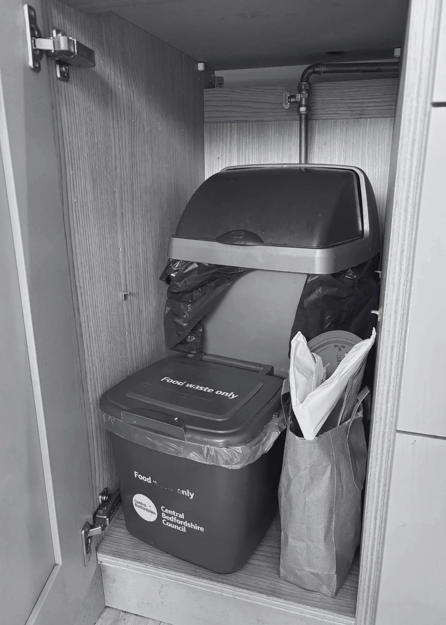 A kitchen cupboard with a small bin, food waste bin and recycling inside it.