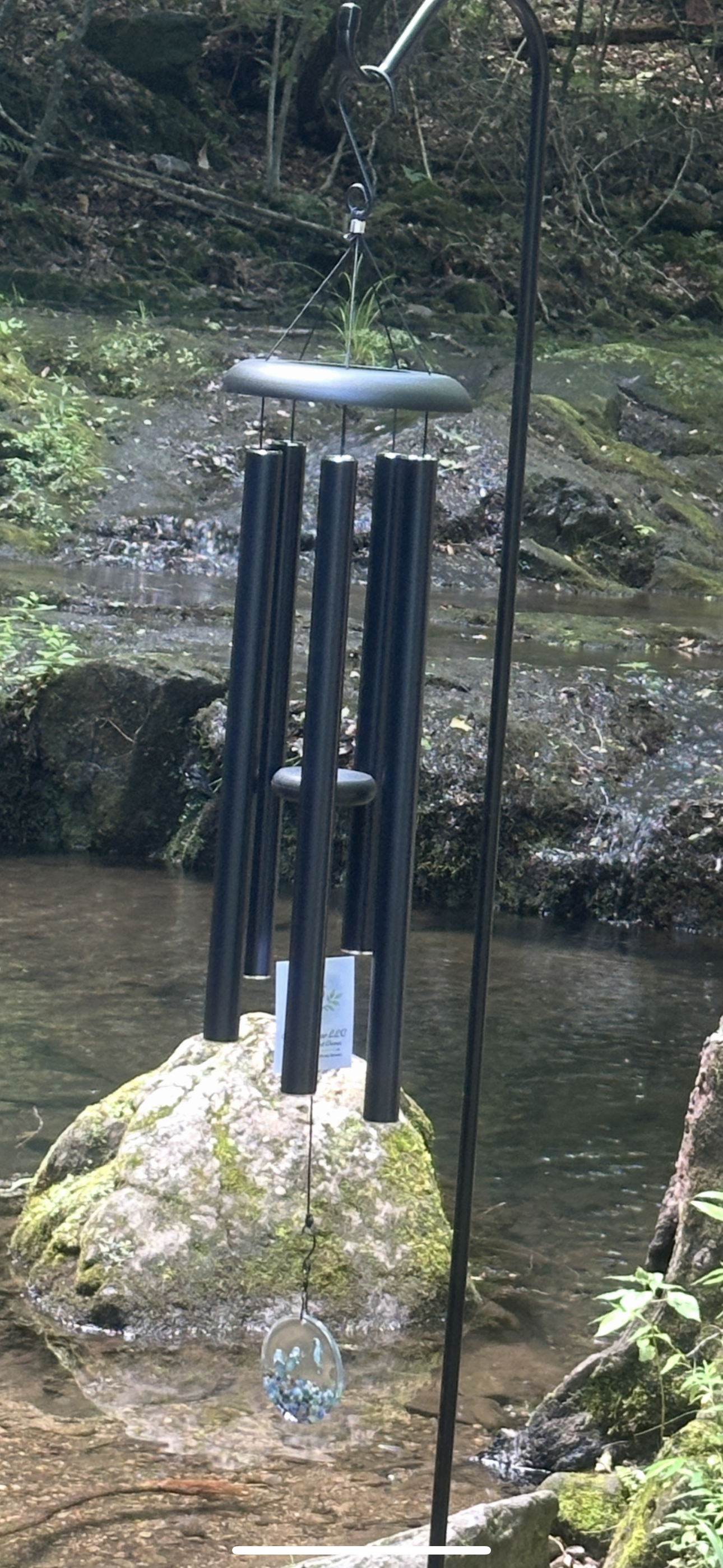 Forever Near wind chime hanging over a scenic forested stream.