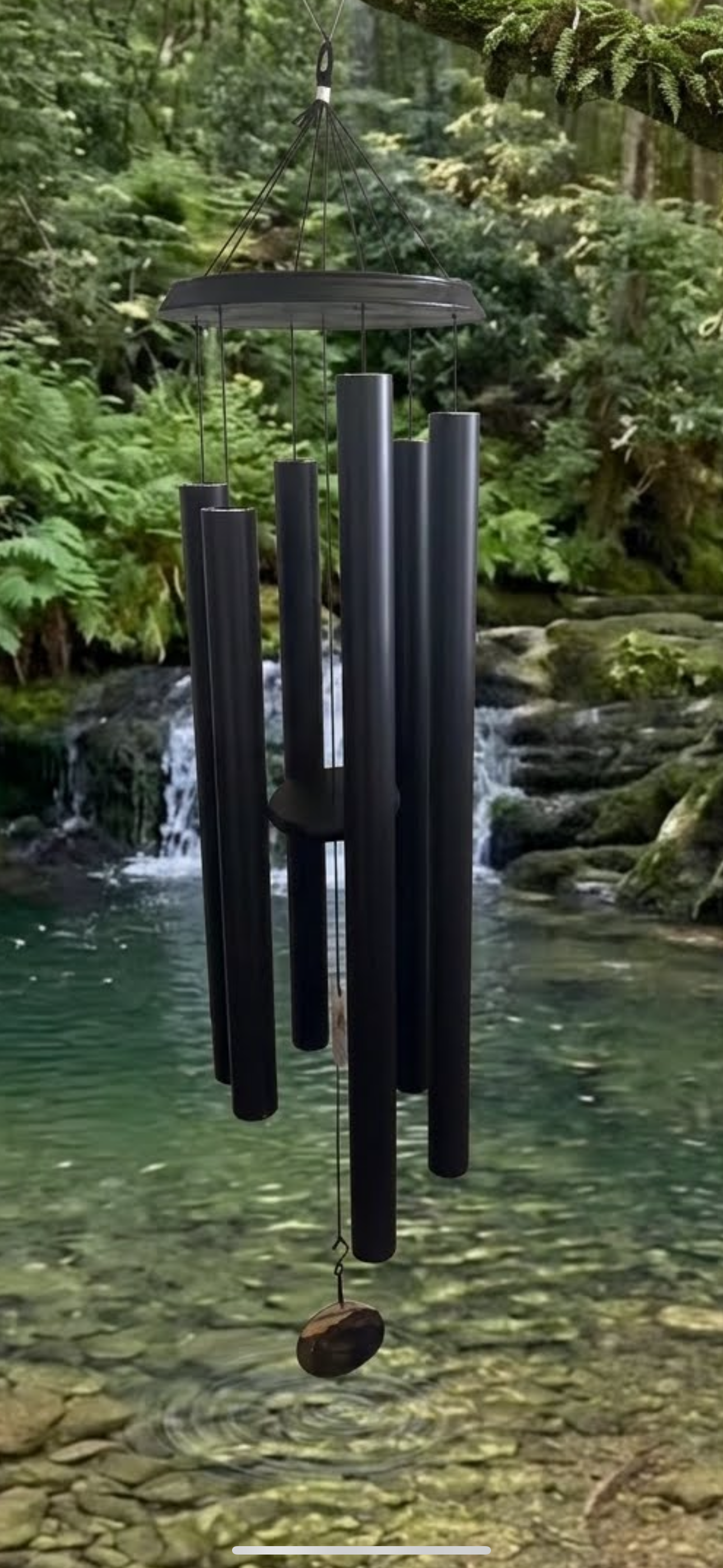 Premium black wind chime swinging gently over a flowing creek.