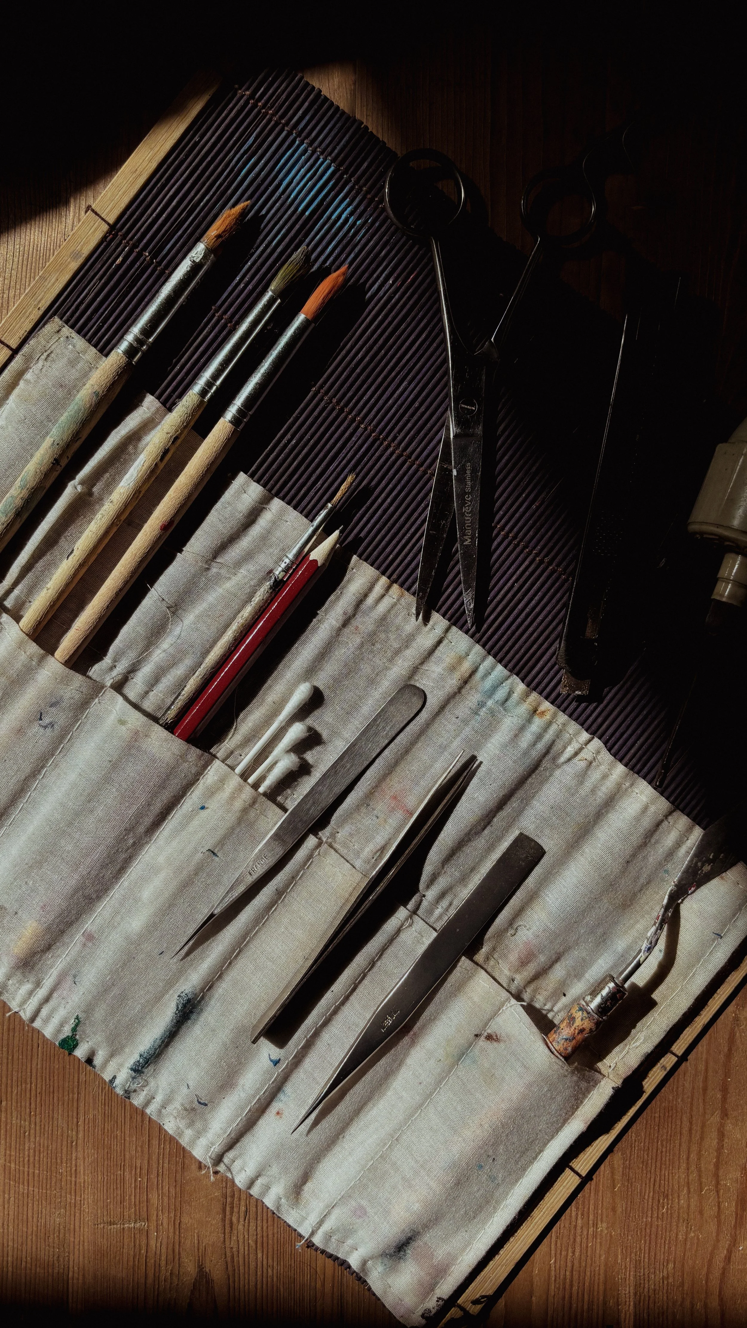 Paintbrushes, scissors, and carving tools laid out on a fabric-covered workspace.