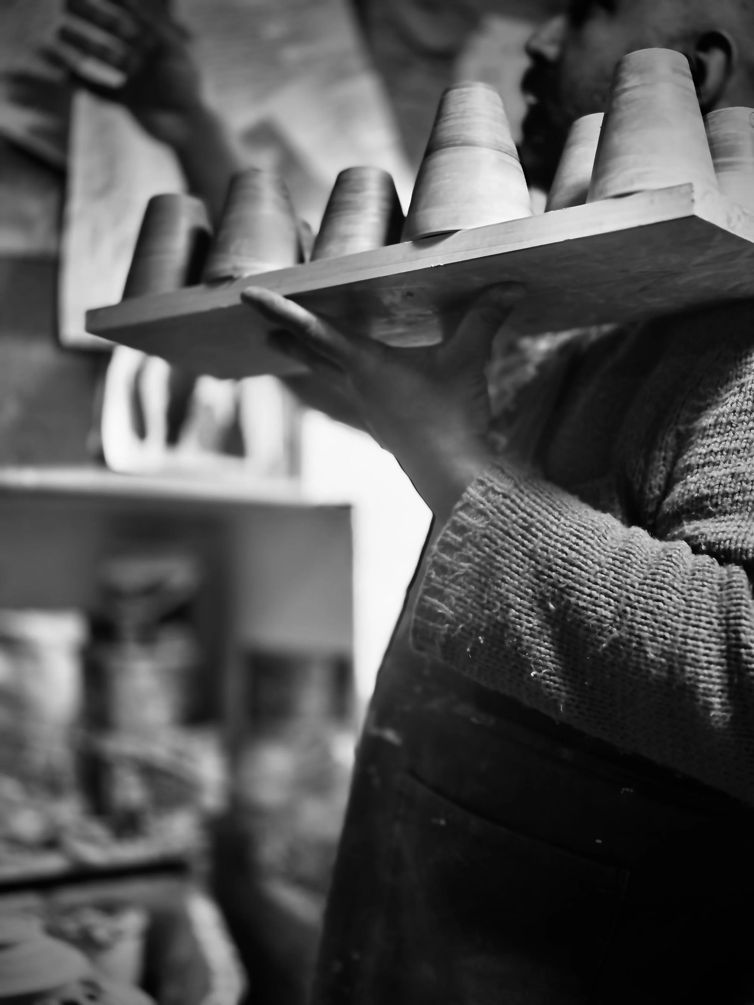 A person holding a wooden board with four upside-down clay pots on top, in a workshop setting.