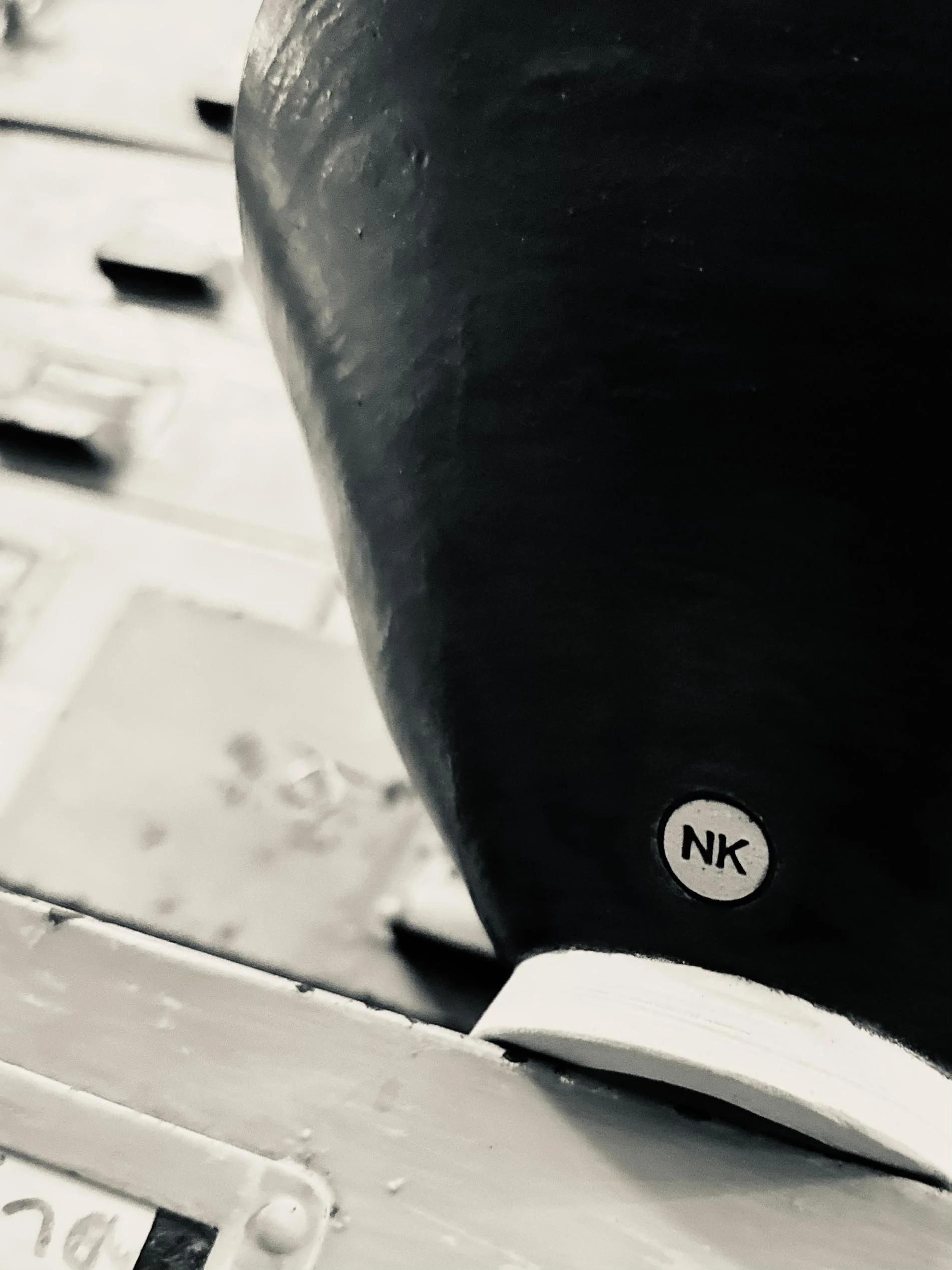 Close-up black object with white sticker labeled 'NK' on a metallic surface, with a blurred background of mechanical or industrial equipment.