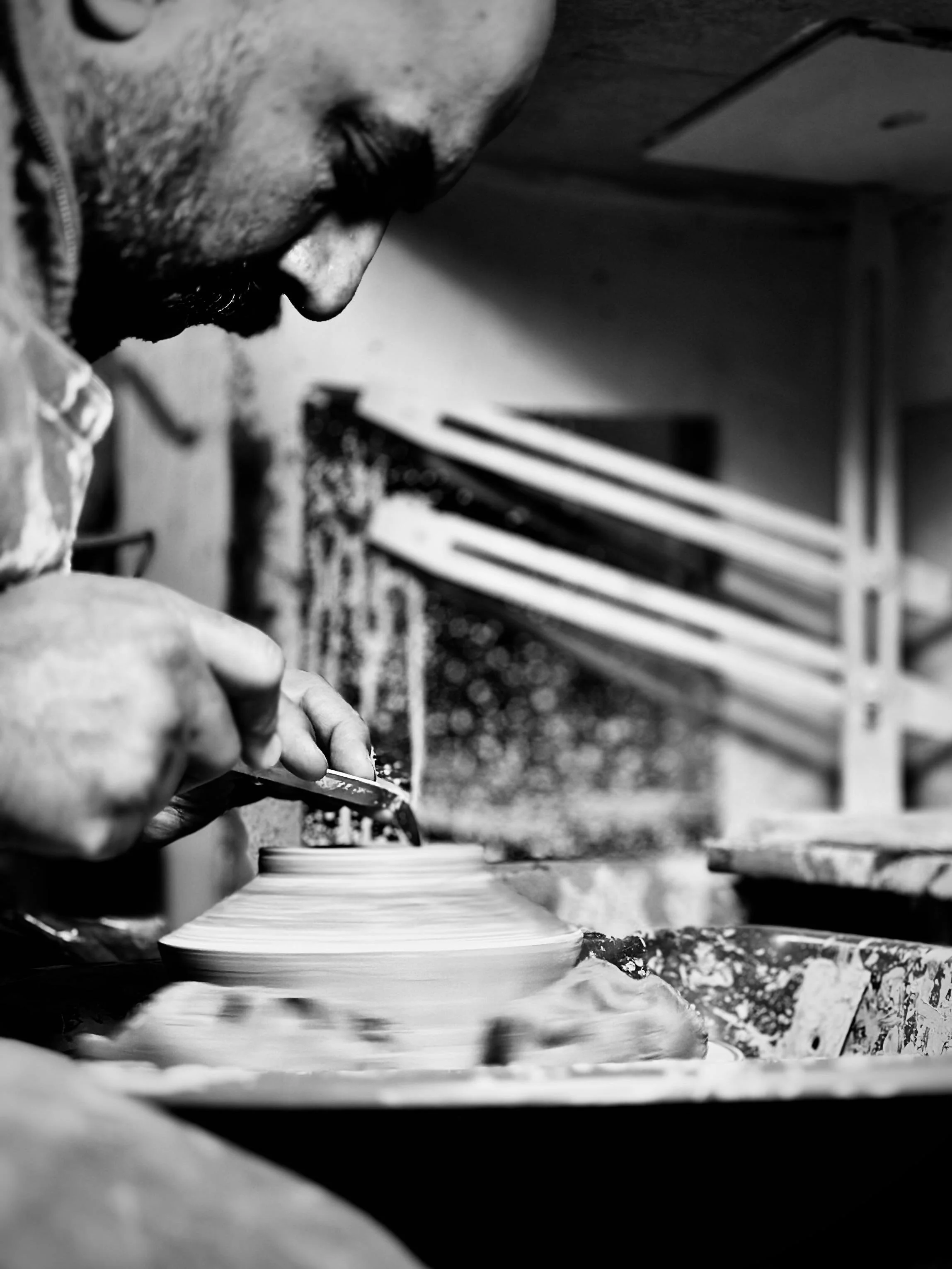 A person carving a ceramic piece on a pottery wheel in a studio.