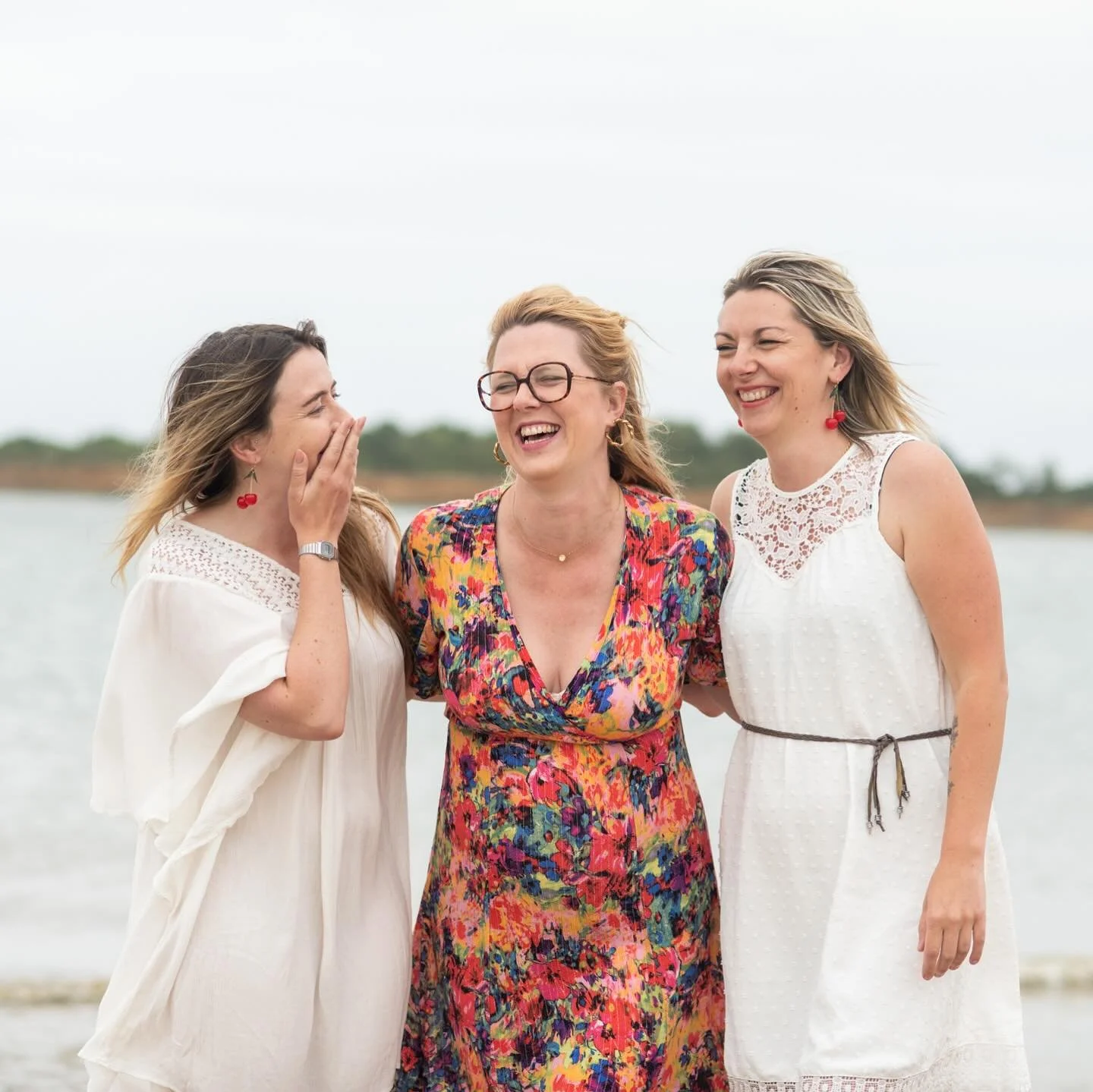 Trois femmes rient ensemble au bord de l'eau lors d'une journée en plein air.