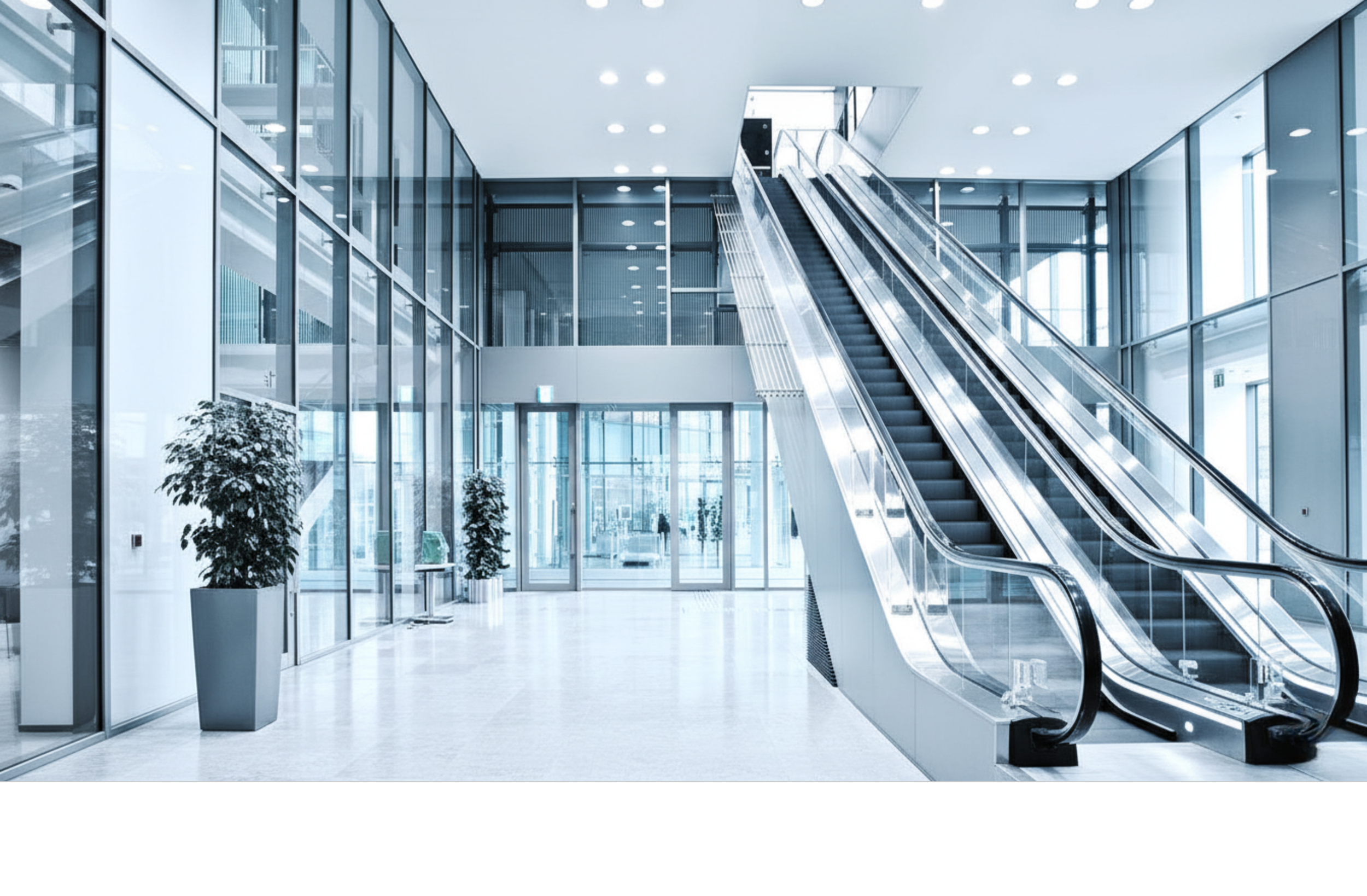 Modern office building lobby with large glass windows, an escalator, and potted plants.