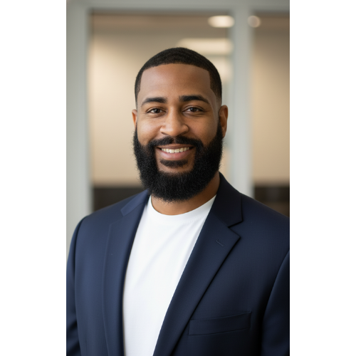 A smiling man with a beard wearing a navy blazer and white shirt in an office setting.