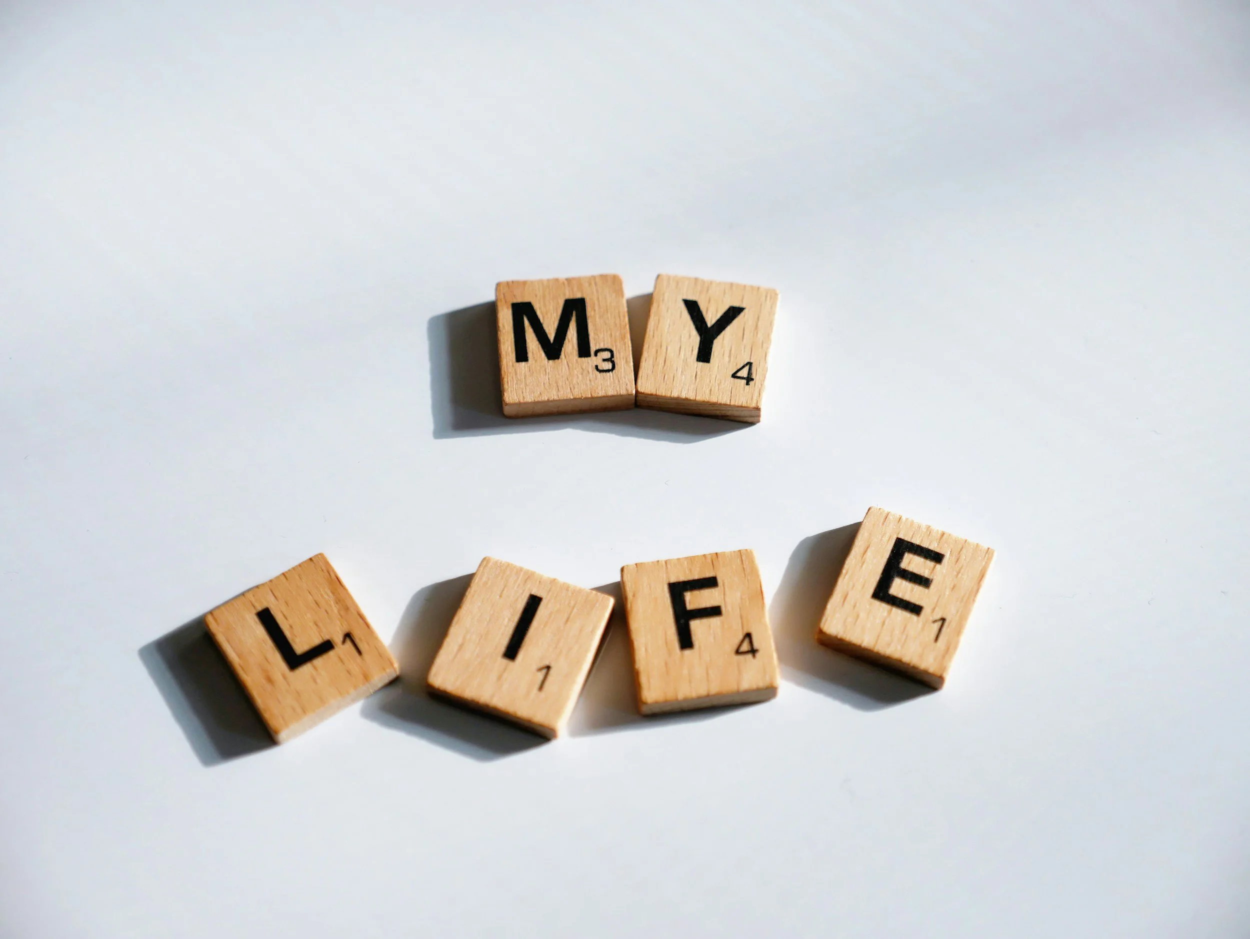 Wooden Scrabble tiles spelling 'M Y' above the tiles spelling 'L I F E' on a white background.
