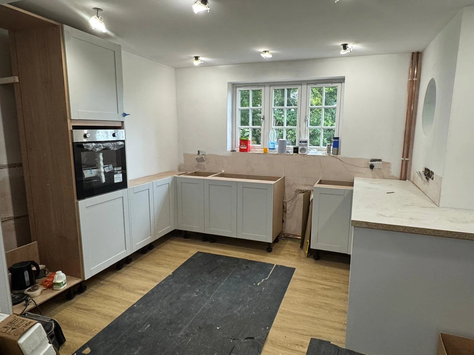Kitchen under renovation with partially installed cabinets, a black oven, construction tools, and a window with green trees outside.