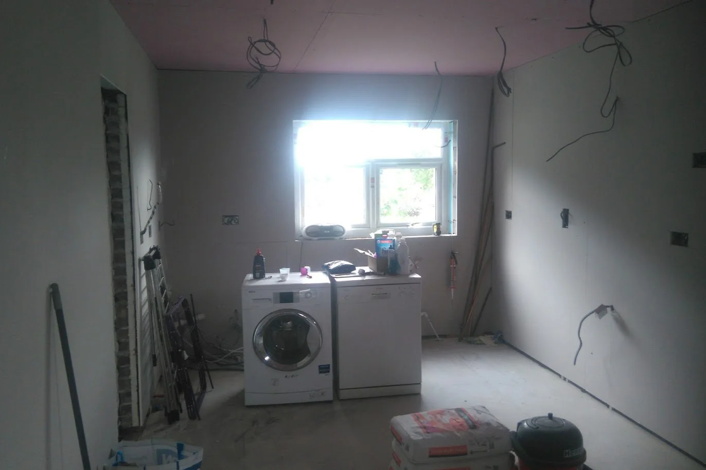 Room under renovation with washer and dryer, construction tools, wires hanging from ceiling, and unfinished walls.